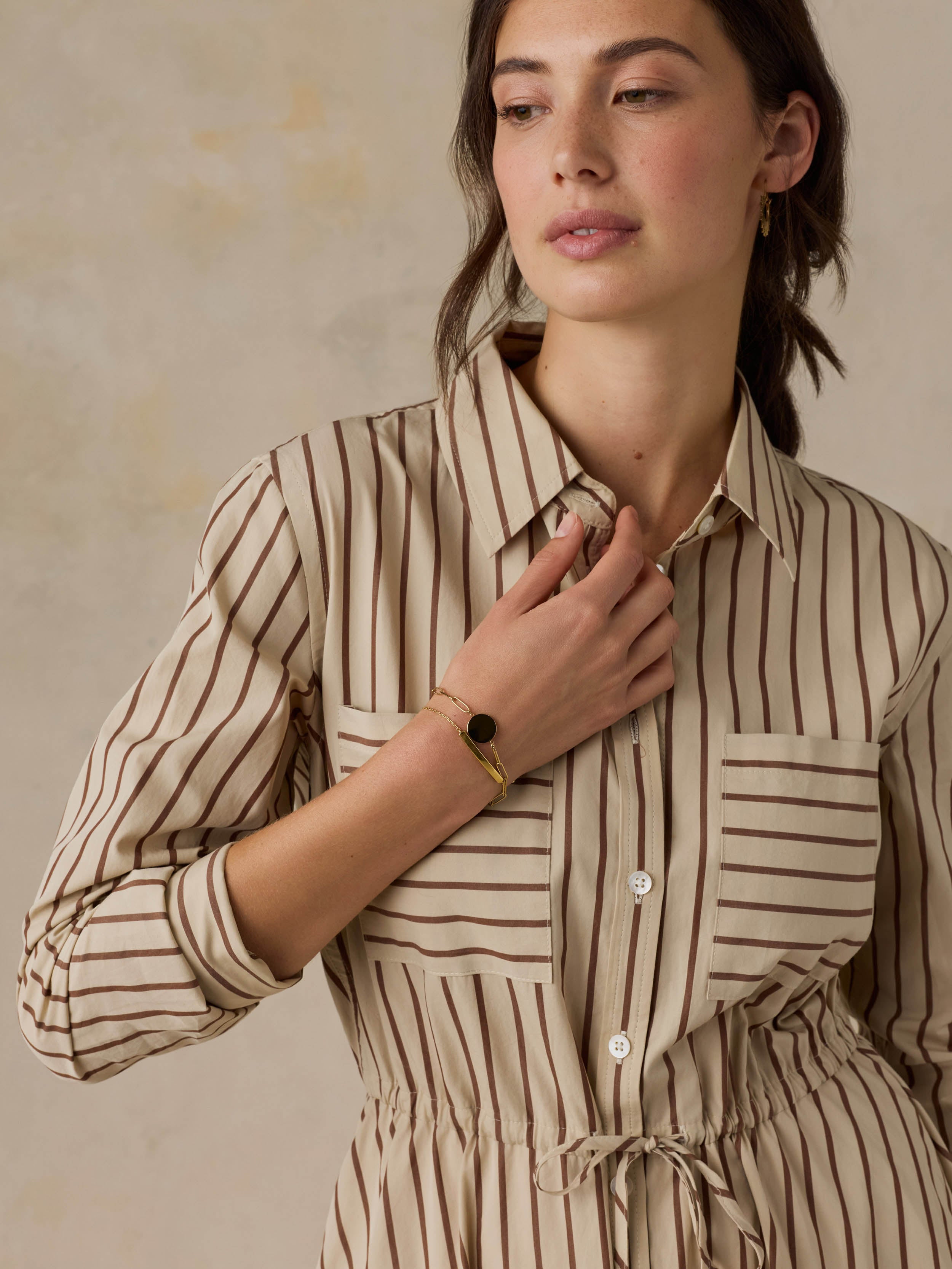 Woman wearing a tan striped dress against a beige background