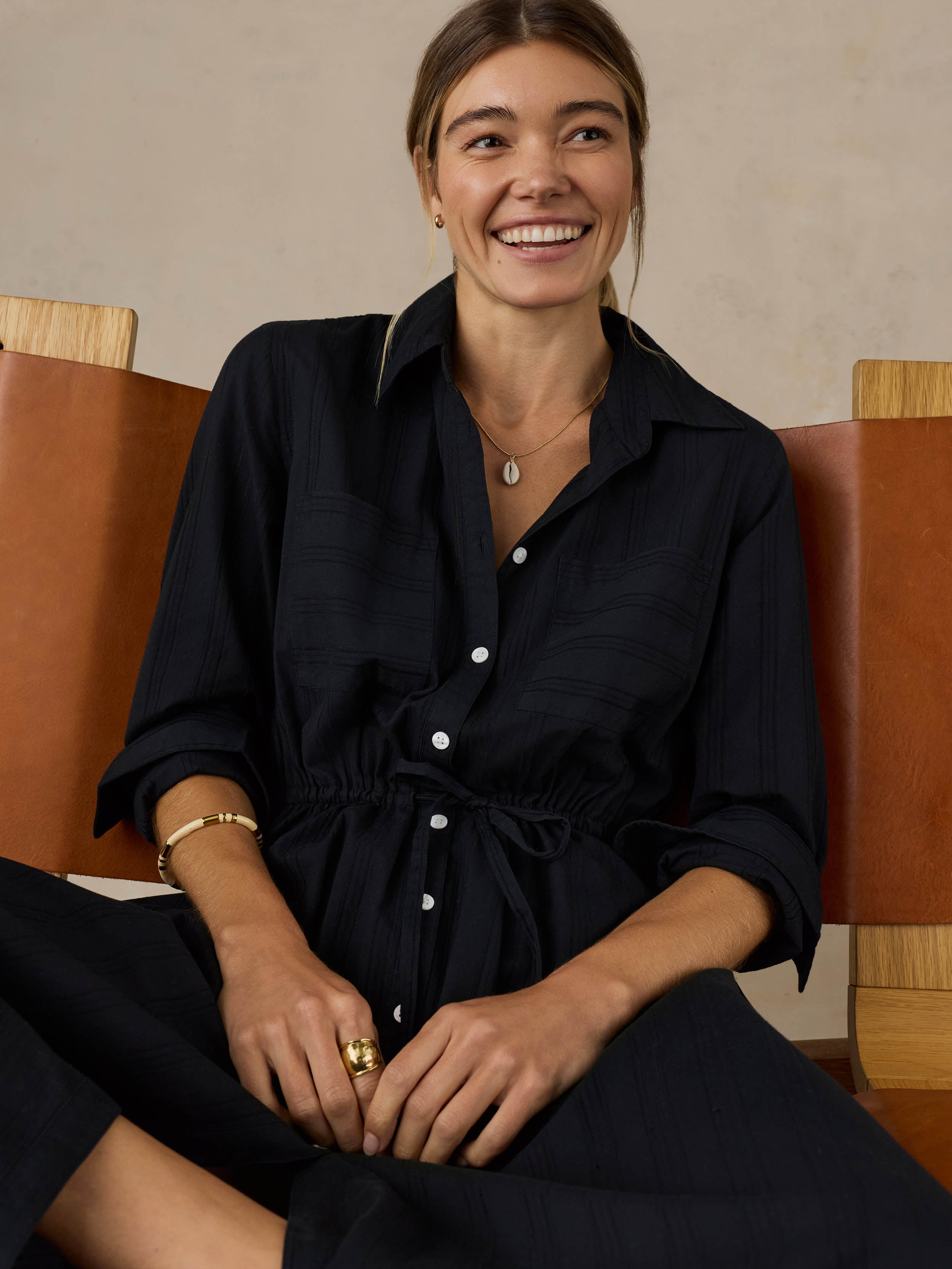 Woman sitting on a wooden chair wearing a black dress against a beige background