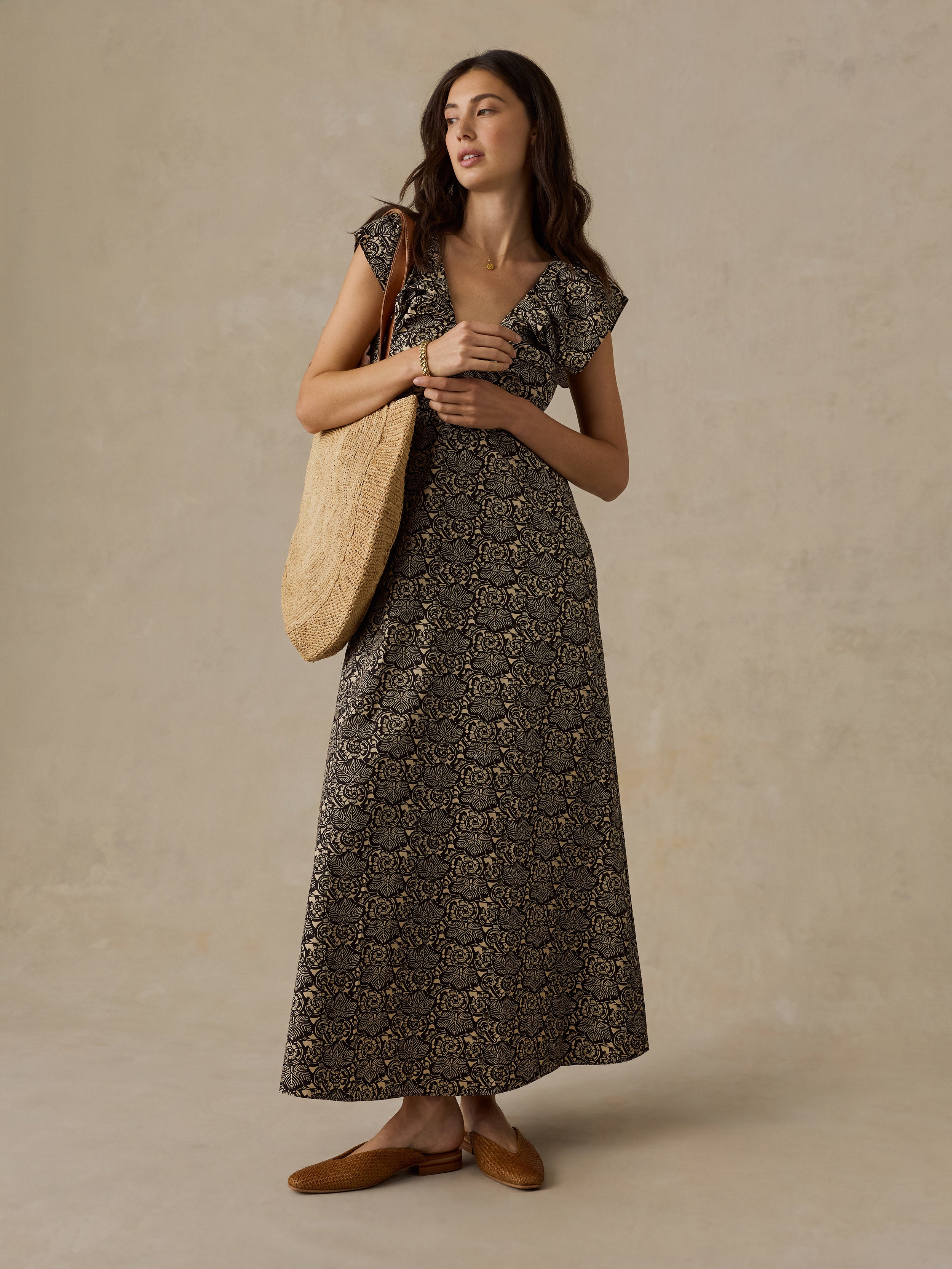 Woman wearing a black and beige floral printed dress and raffia bag against a beige background