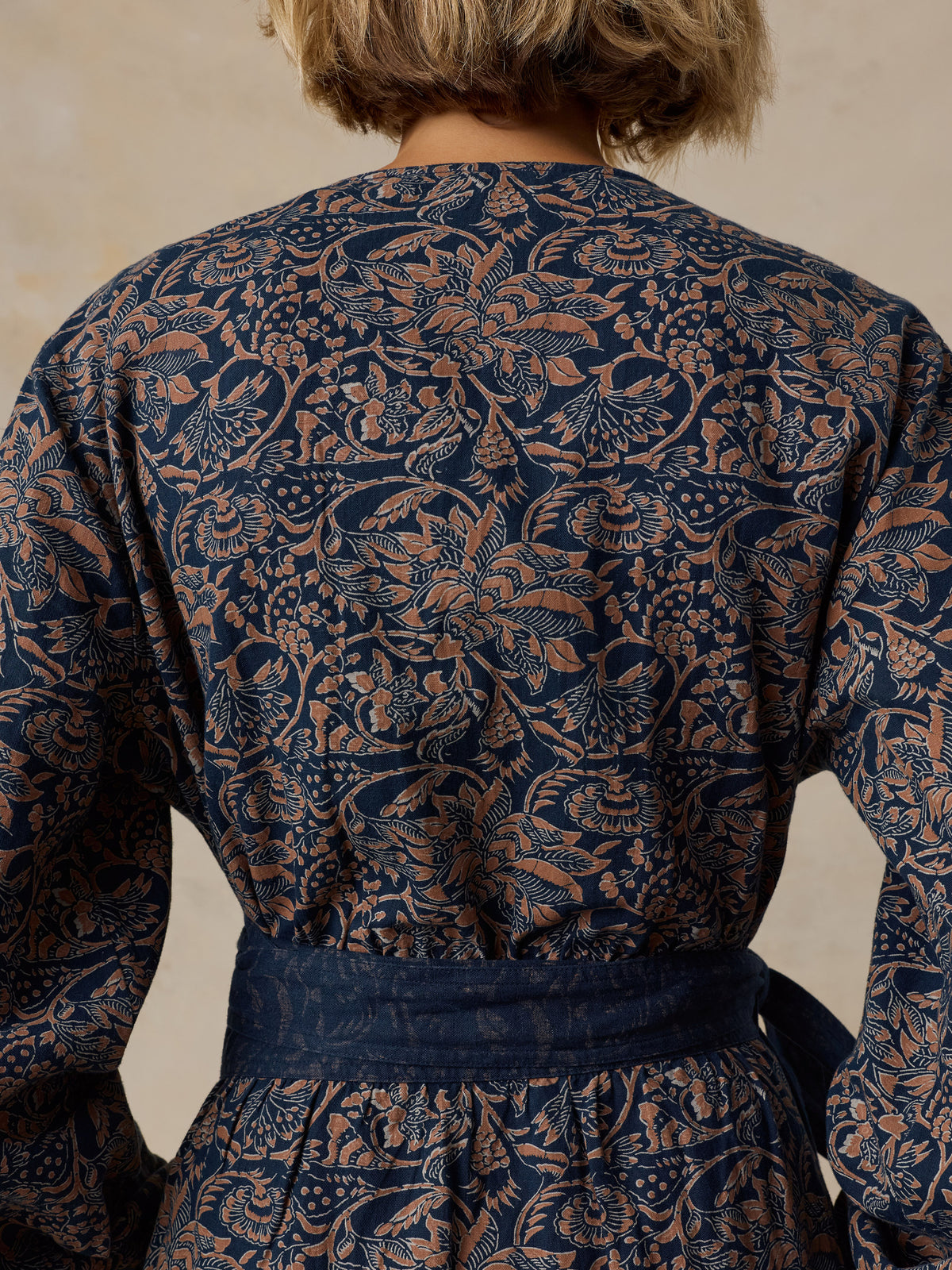 A close-up of a woman wearing a navy blue shirt dress with a rust-orange floral block print pattern, featuring a button-down front, collar, and self-tie waist belt., image 4 of 5