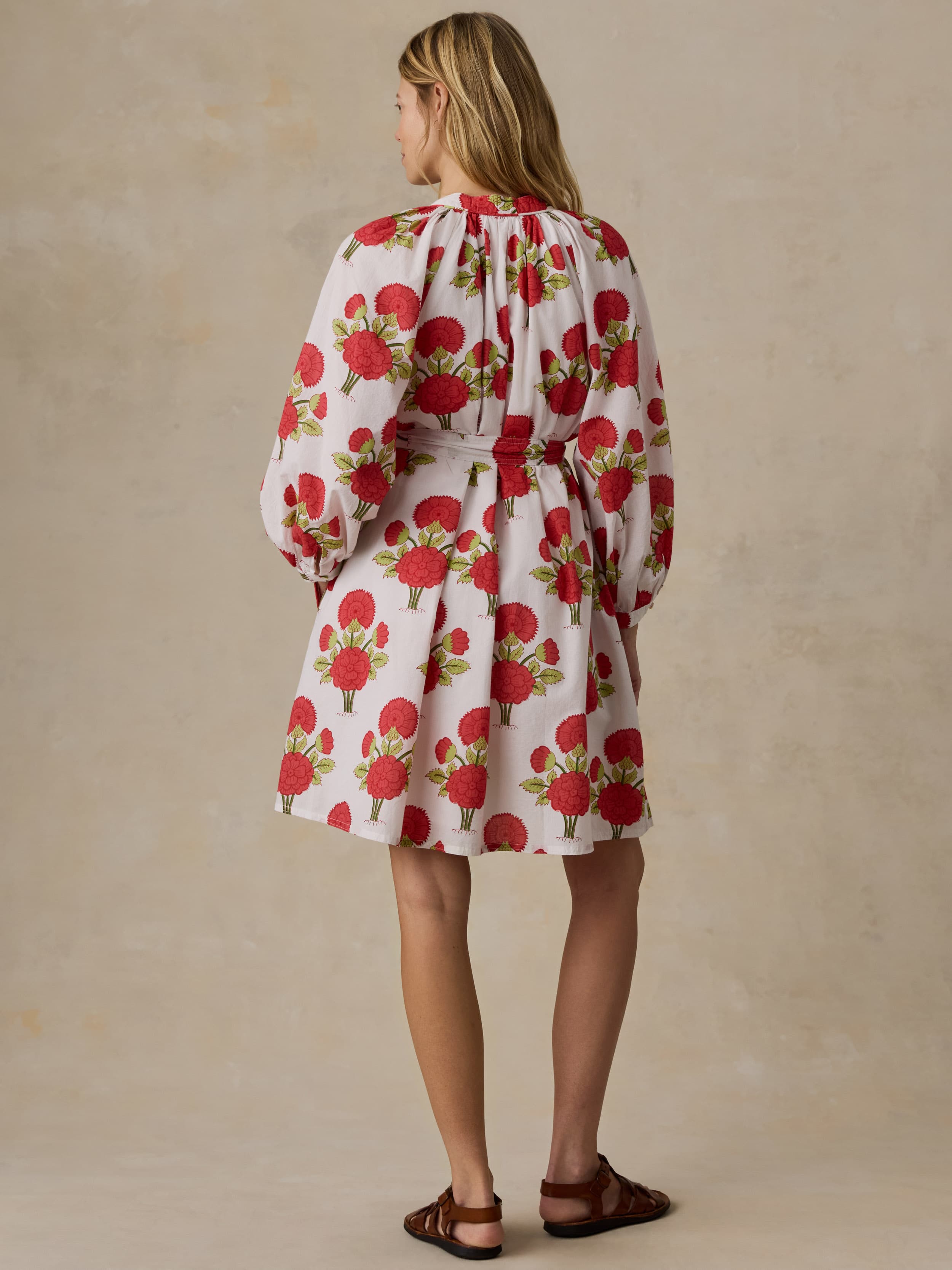 Woman wearing a white dress with red floral patterns on a beige background