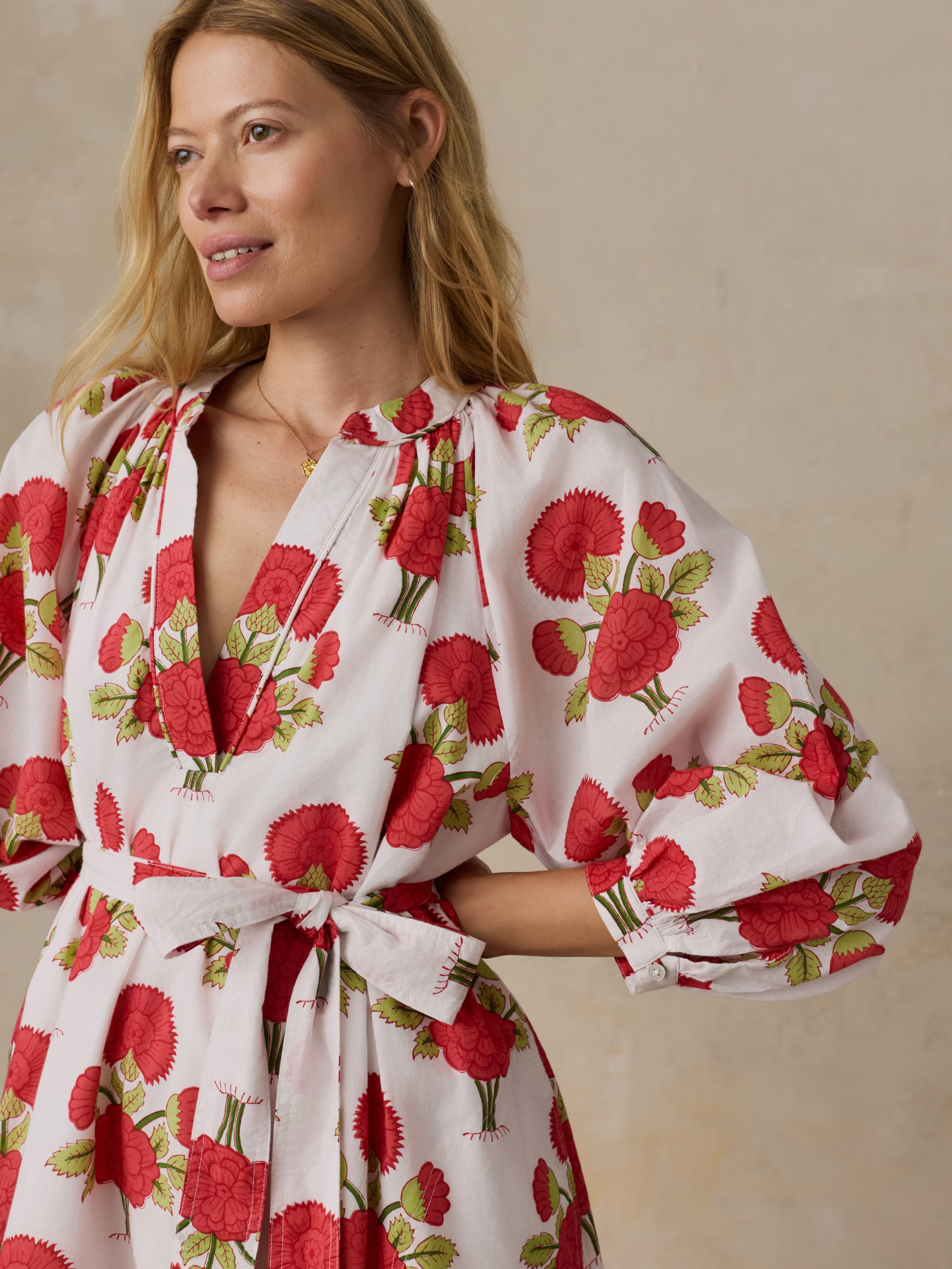 Woman wearing a white dress with red floral patterns on a beige background