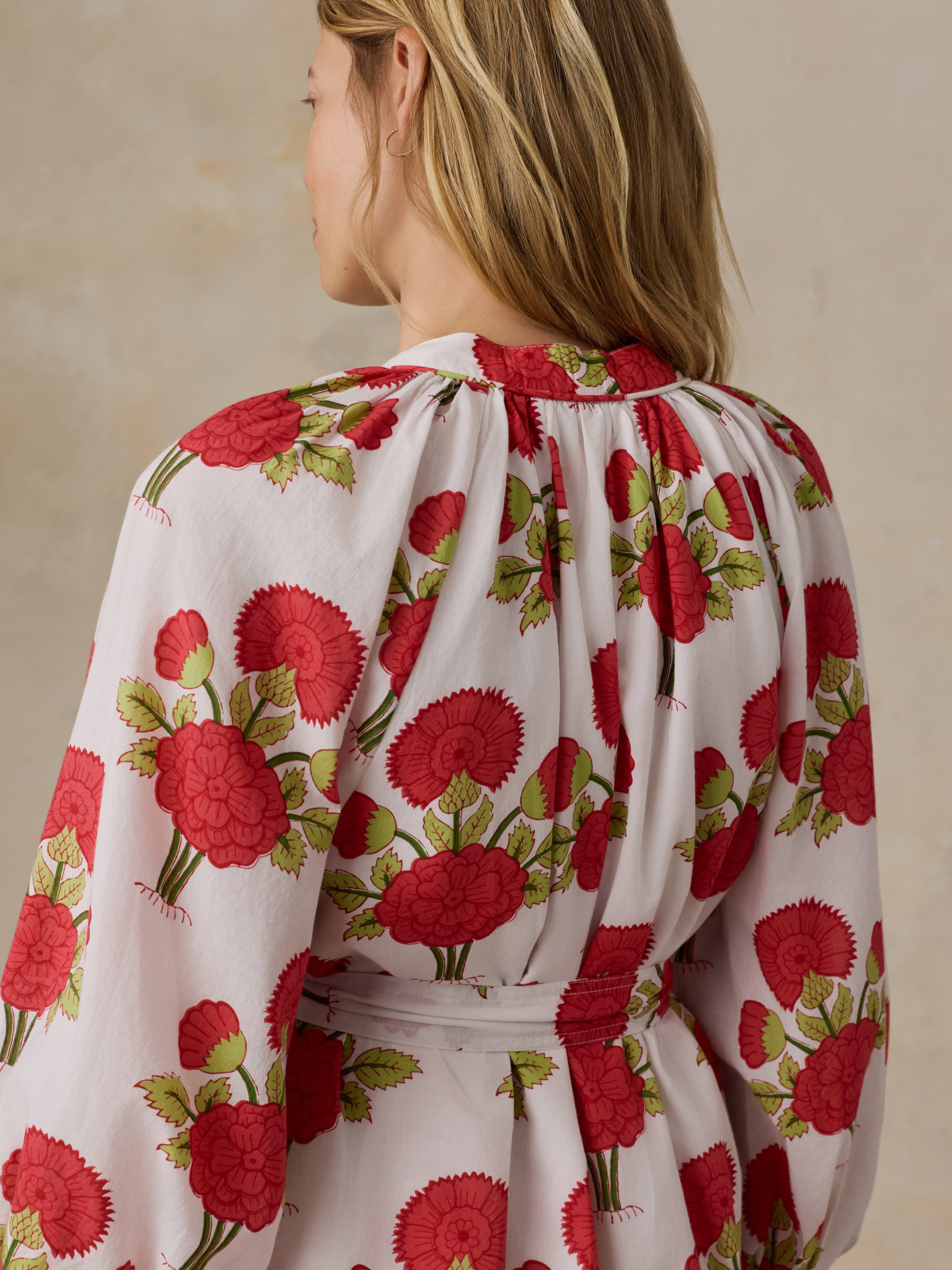 Woman wearing a white dress with red floral patterns on a beige background