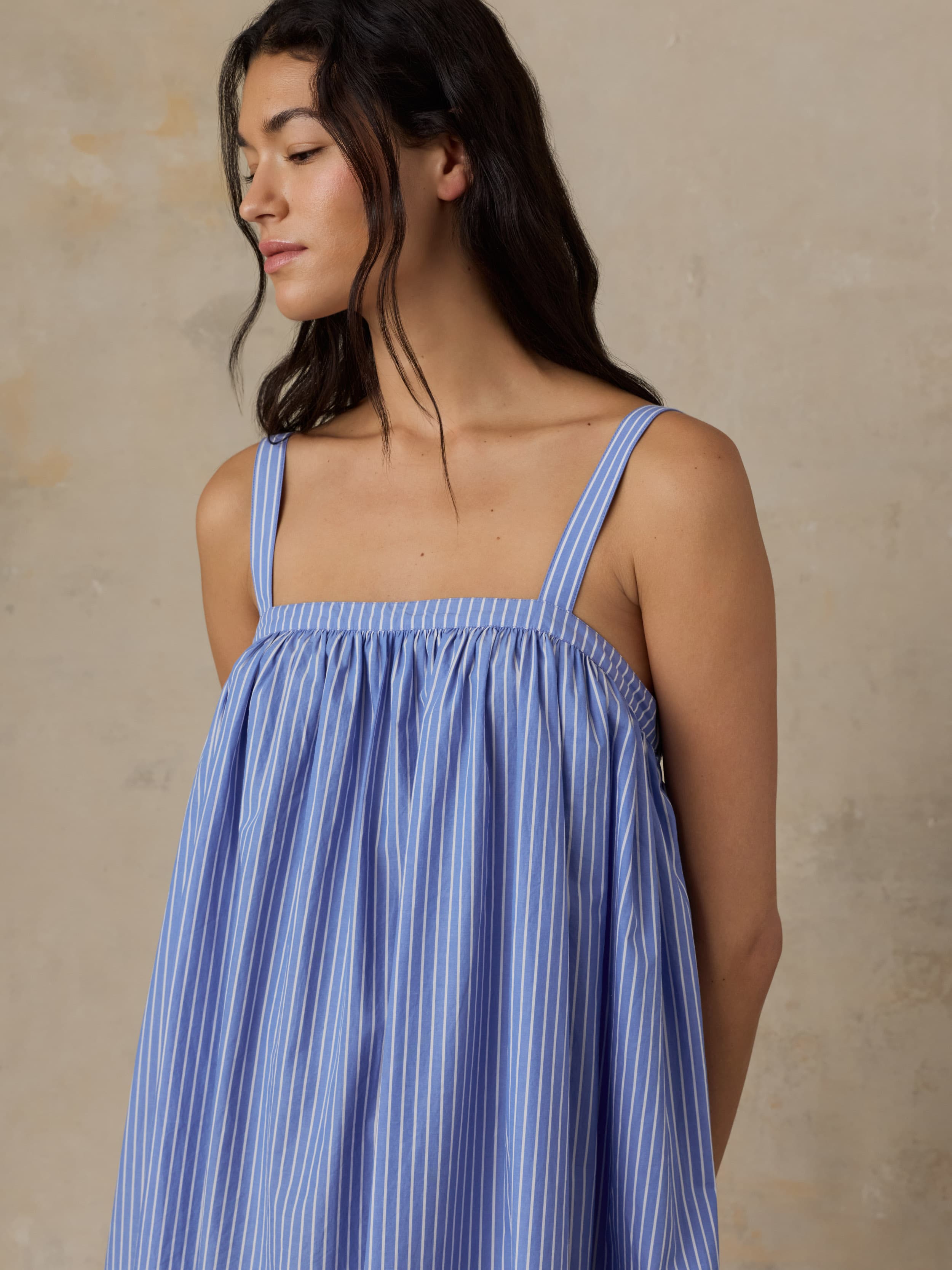 Woman wearing a blue striped dress against a beige background