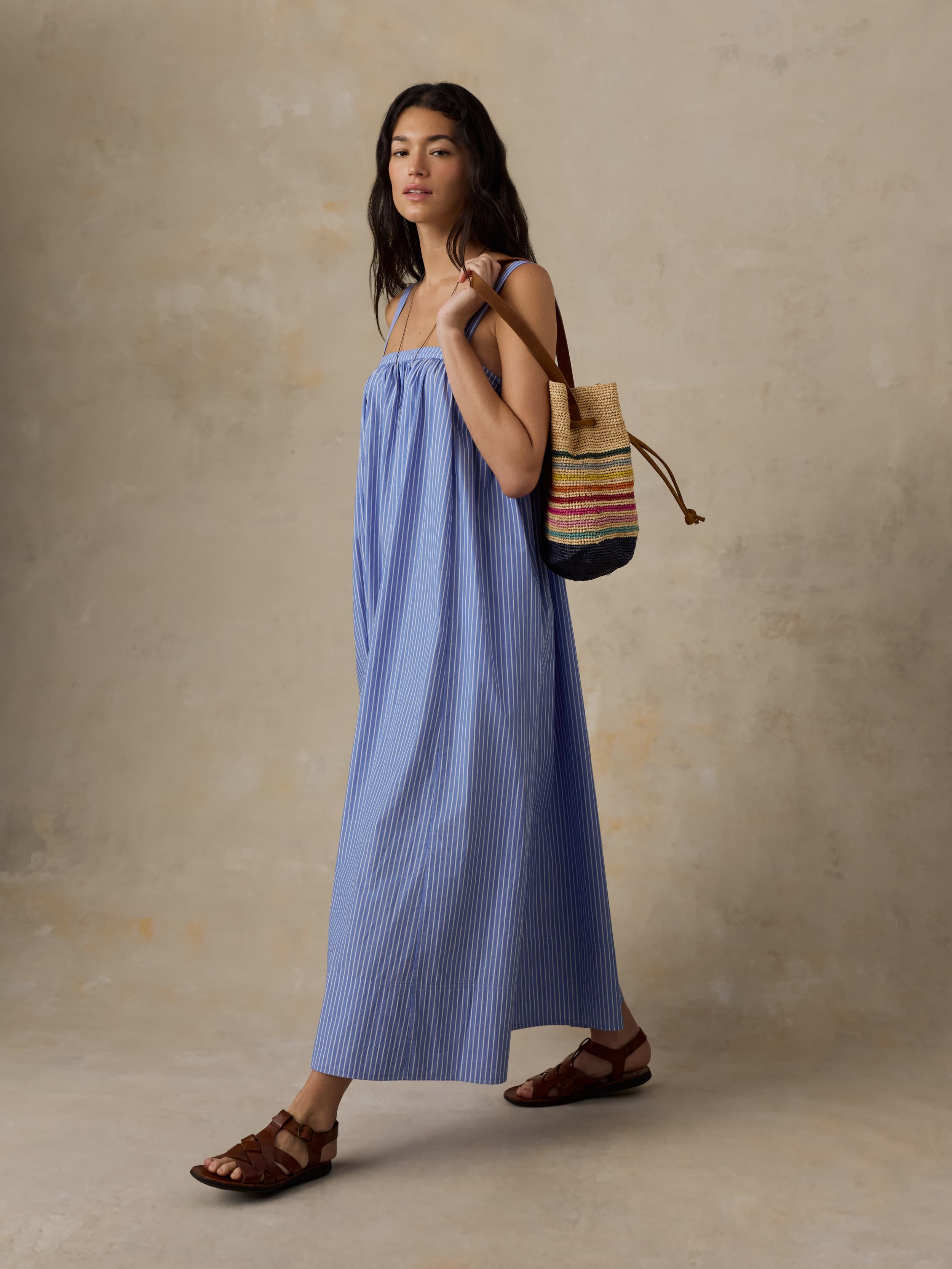 Woman in a blue dress holding a colorful bag against a beige background