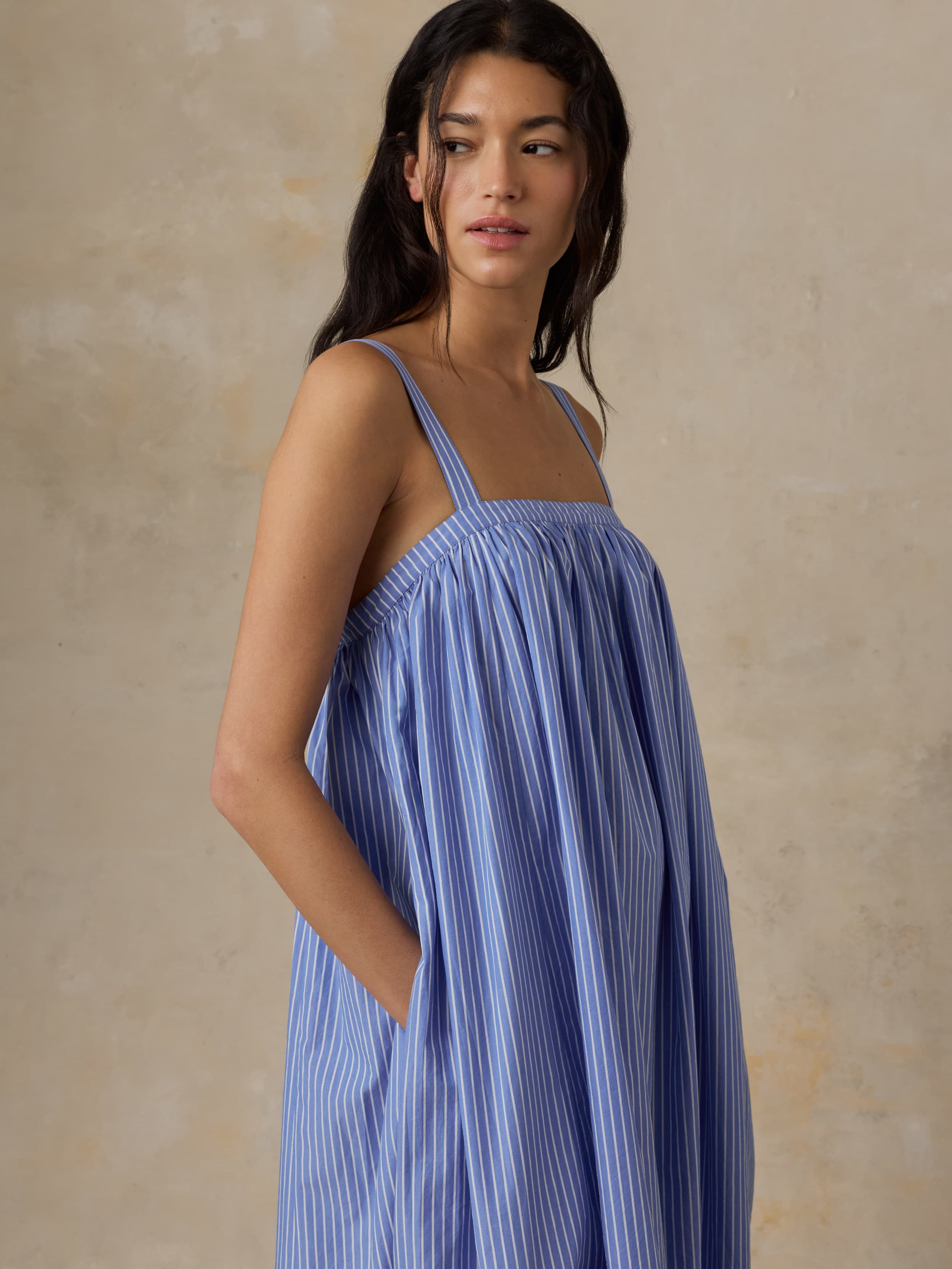Woman wearing a blue striped dress against a beige background