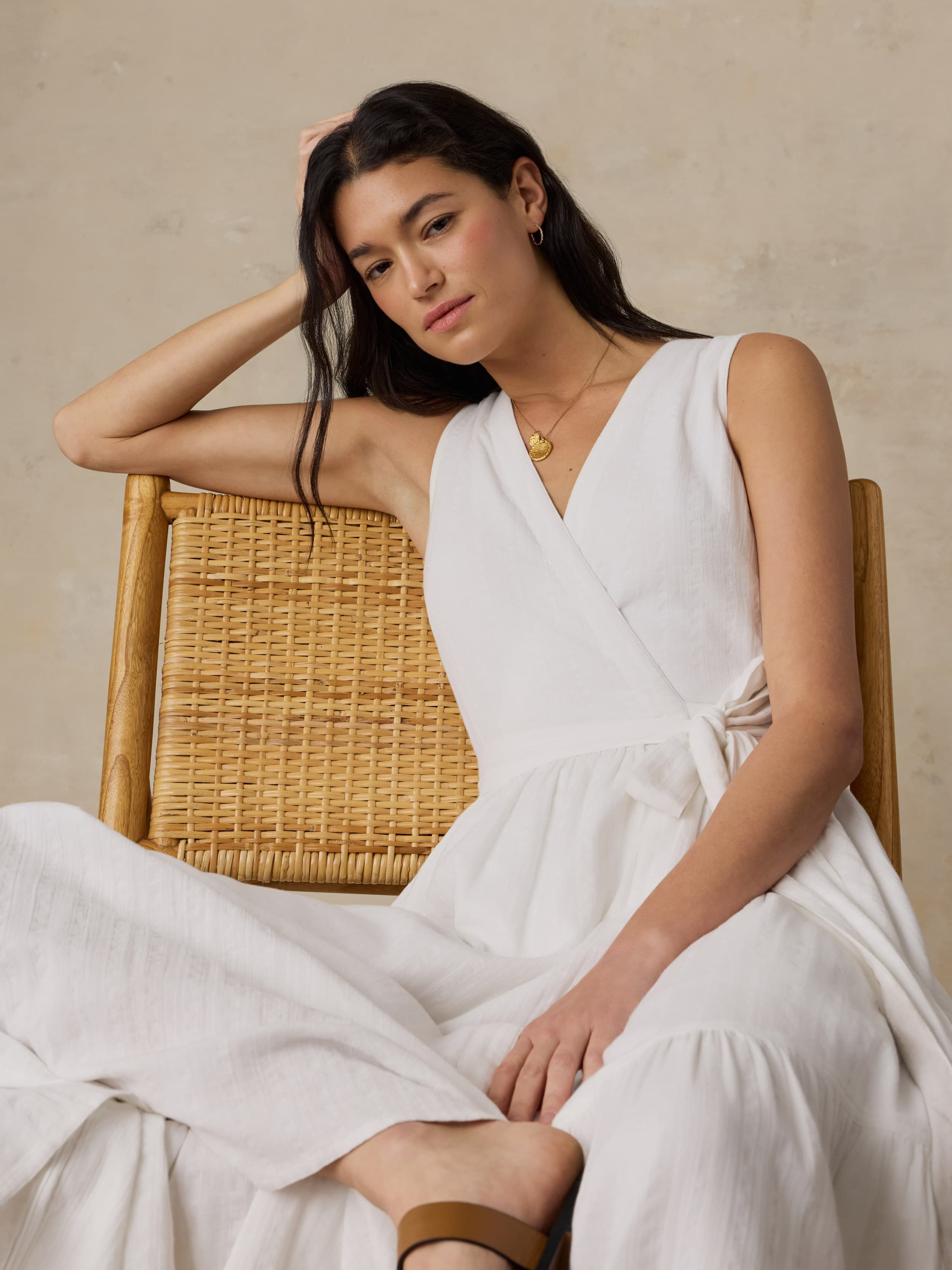 Woman sitting on a wooden chair wearing a white dress against a beige background
