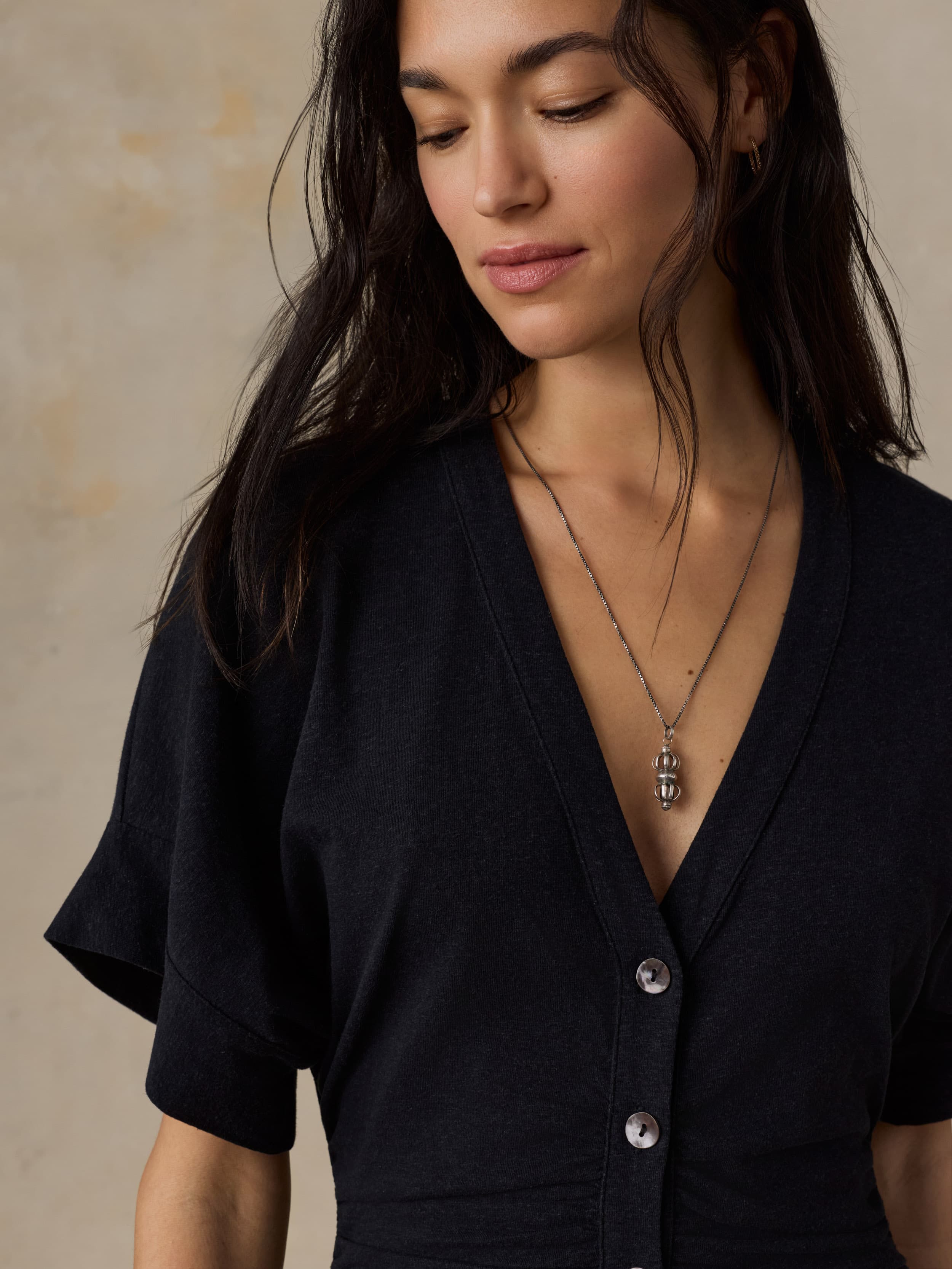 Woman wearing a black dress with a necklace against a beige background