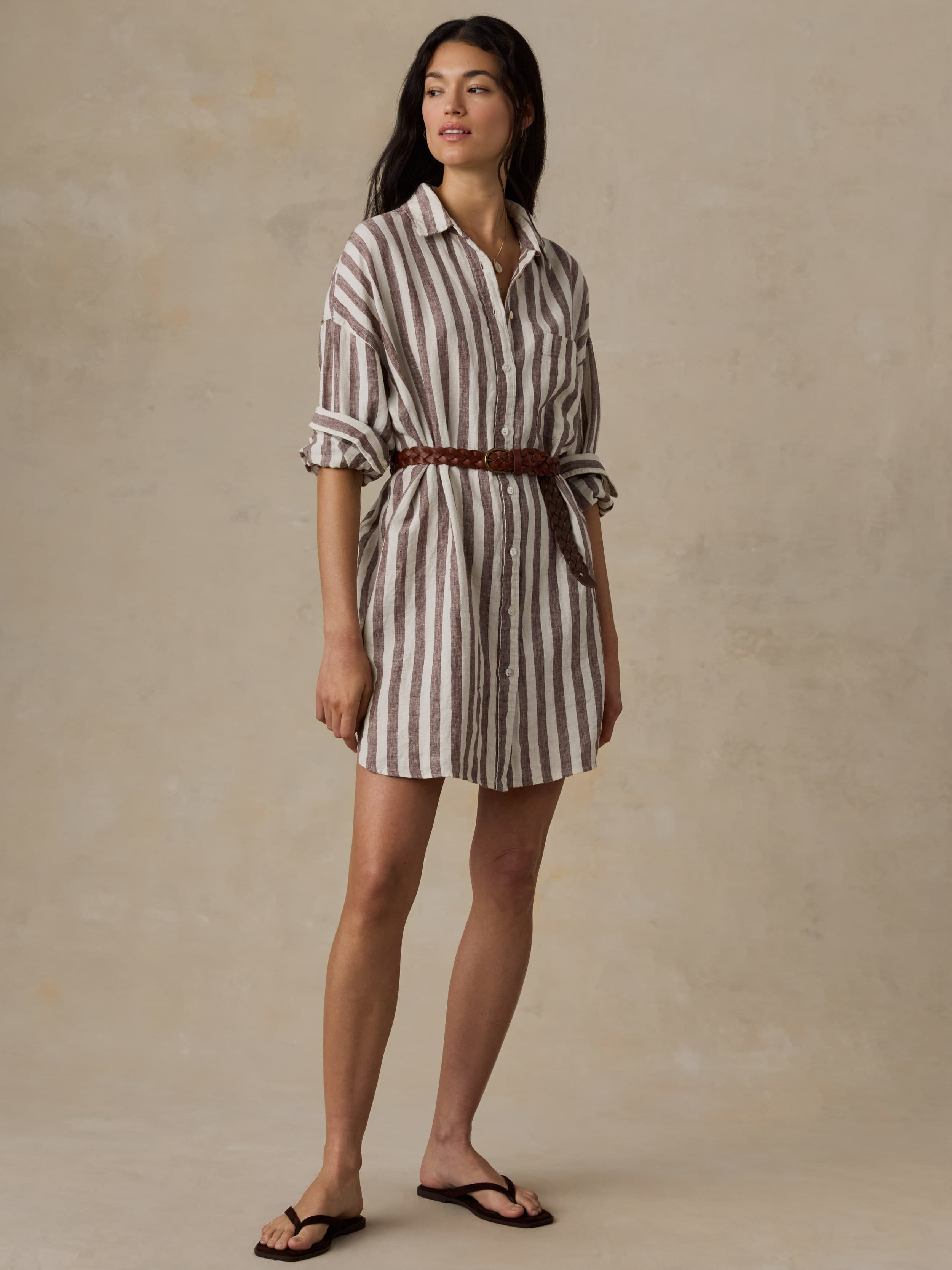 Woman wearing a striped shirt  dress with a belt against a beige background