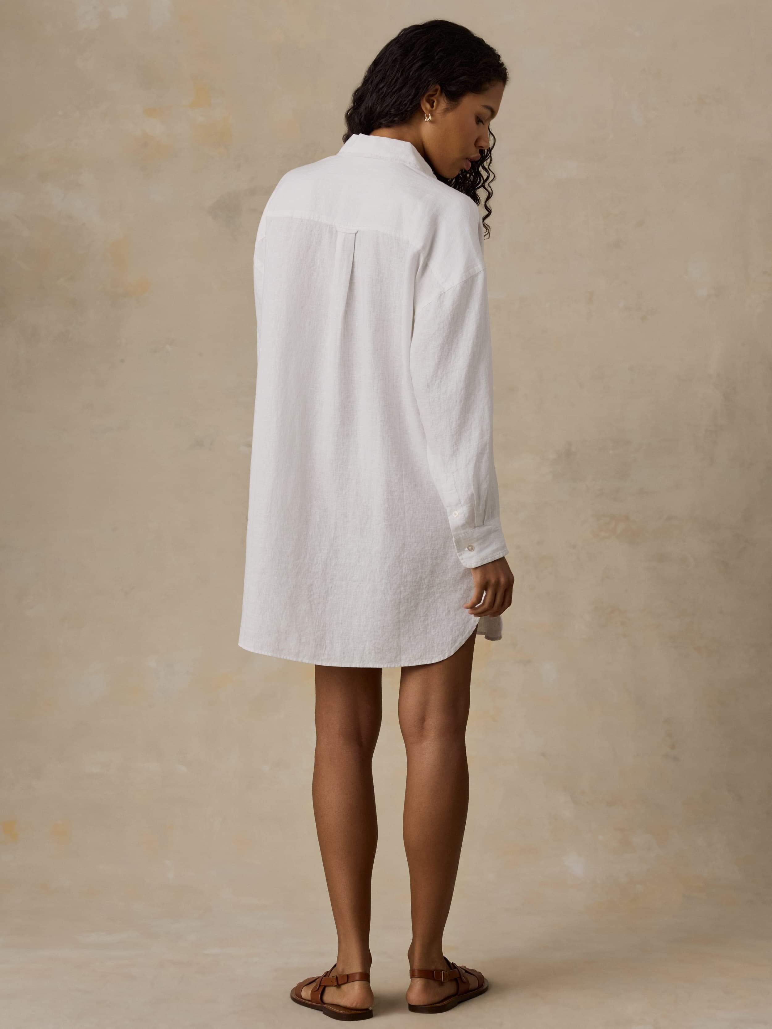 Woman wearing a white shirtdress against a beige background