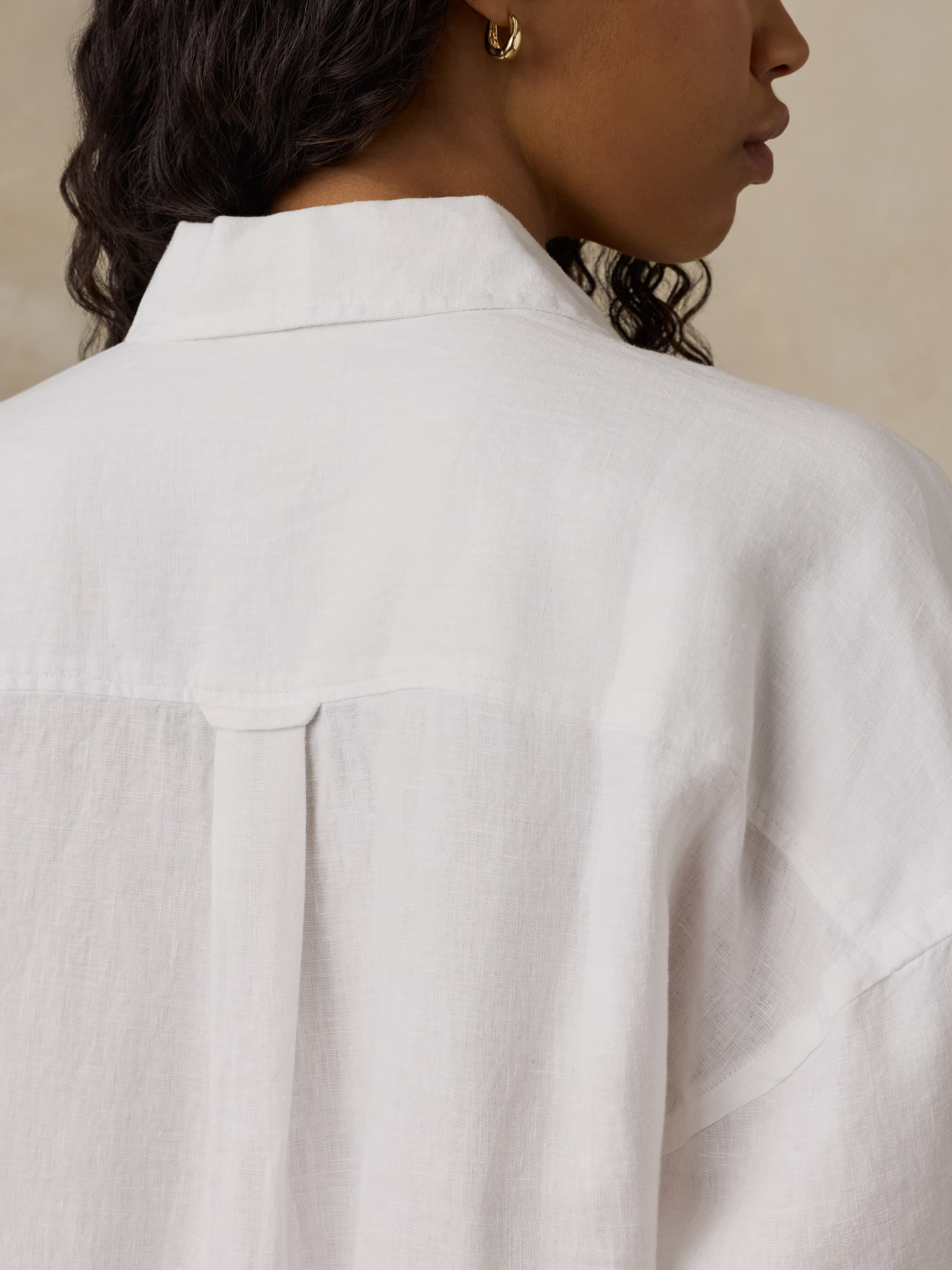 Close-up of a woman wearing a white shirtdress with a neutral background