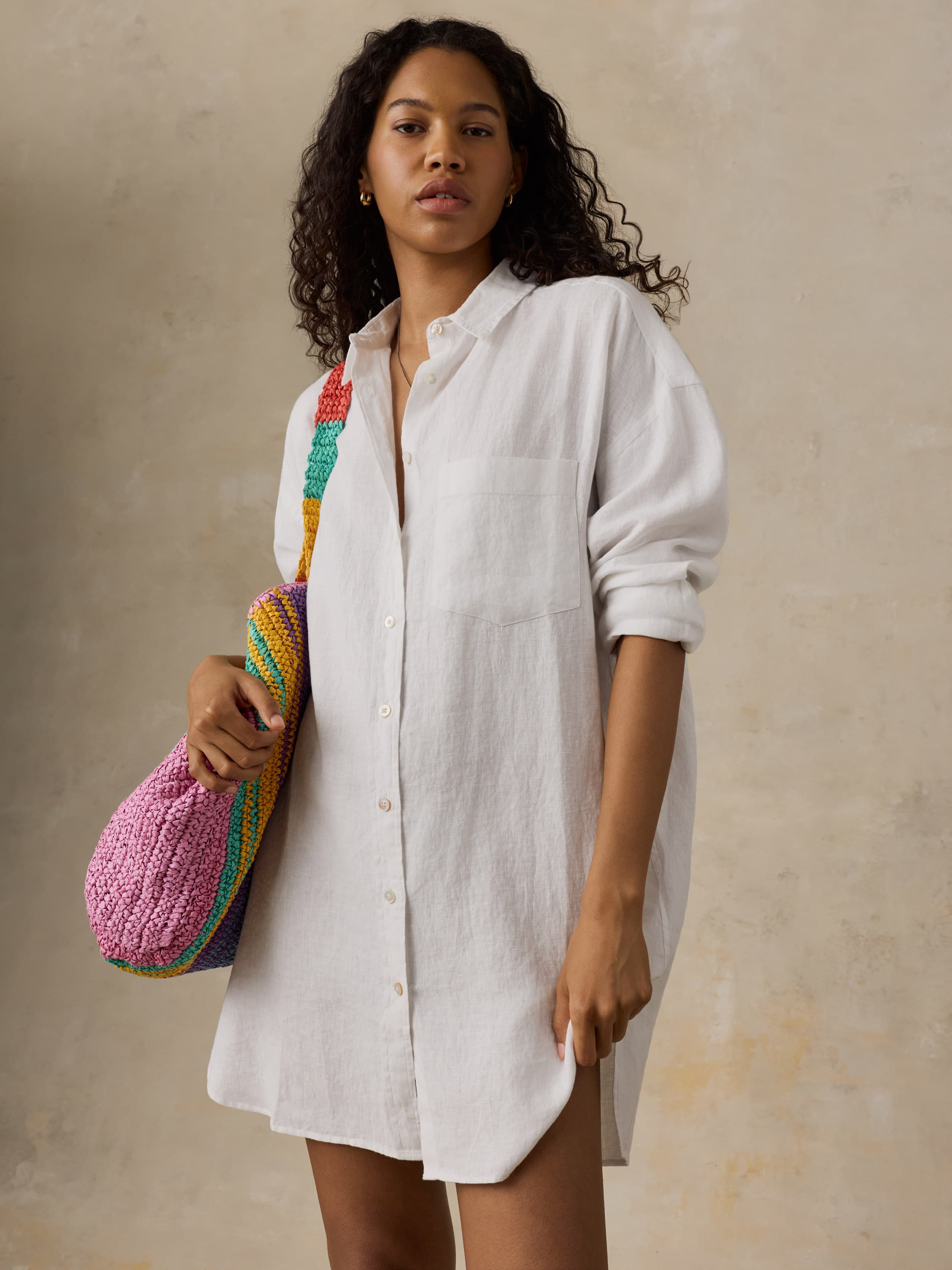 Woman wearing a white shirtdress holding a colorful bag against a beige background