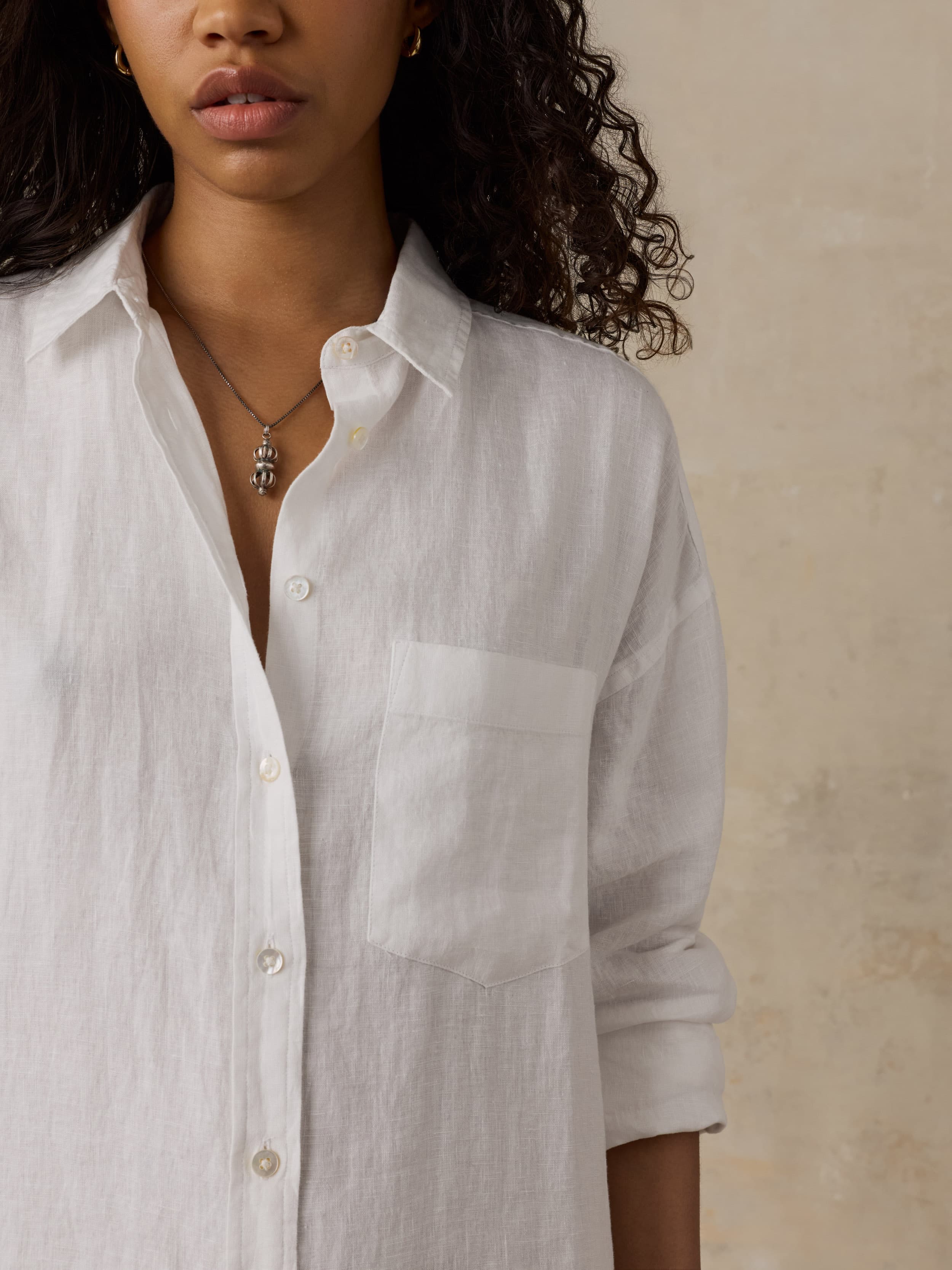 Woman wearing a white linen shirtdress against a beige background