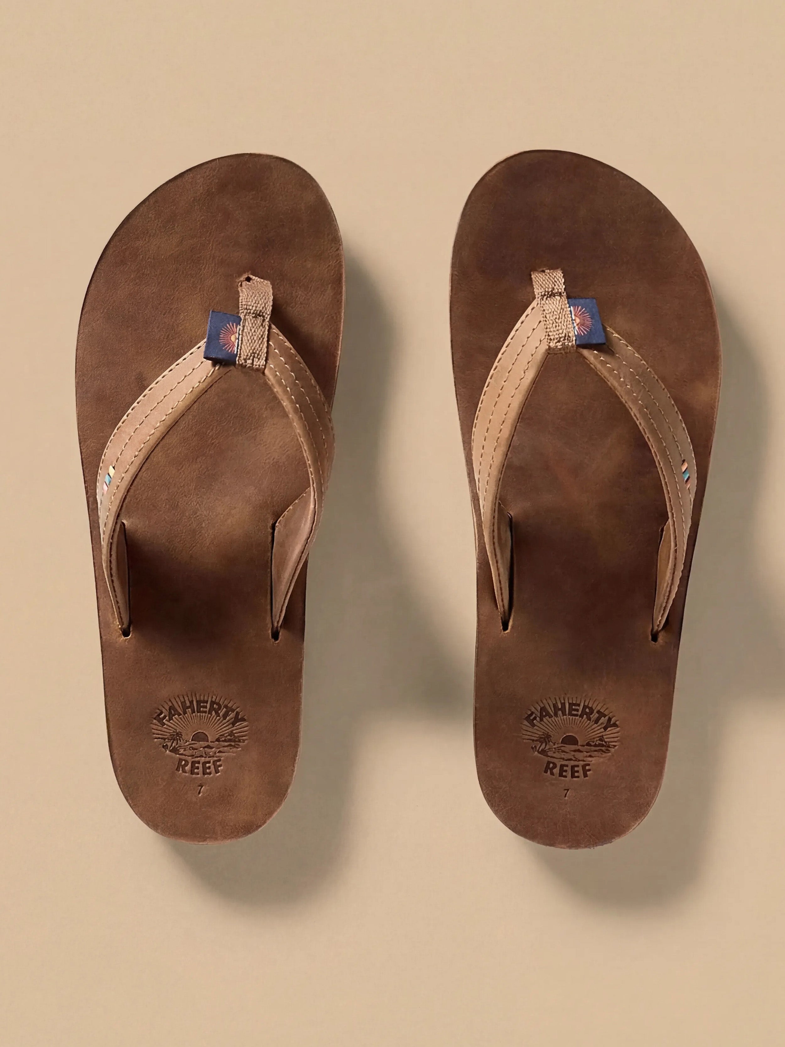 Pair of brown sandals with visible Faherty brand logo on a beige background