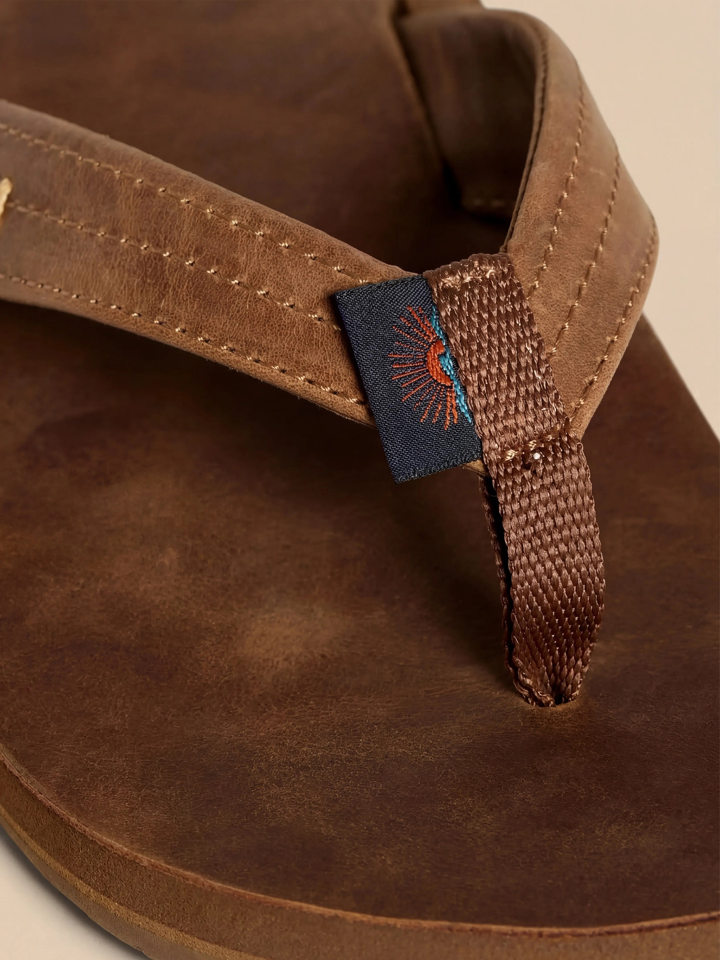 Brown sandal with a Faherty brand tag against a beige background
