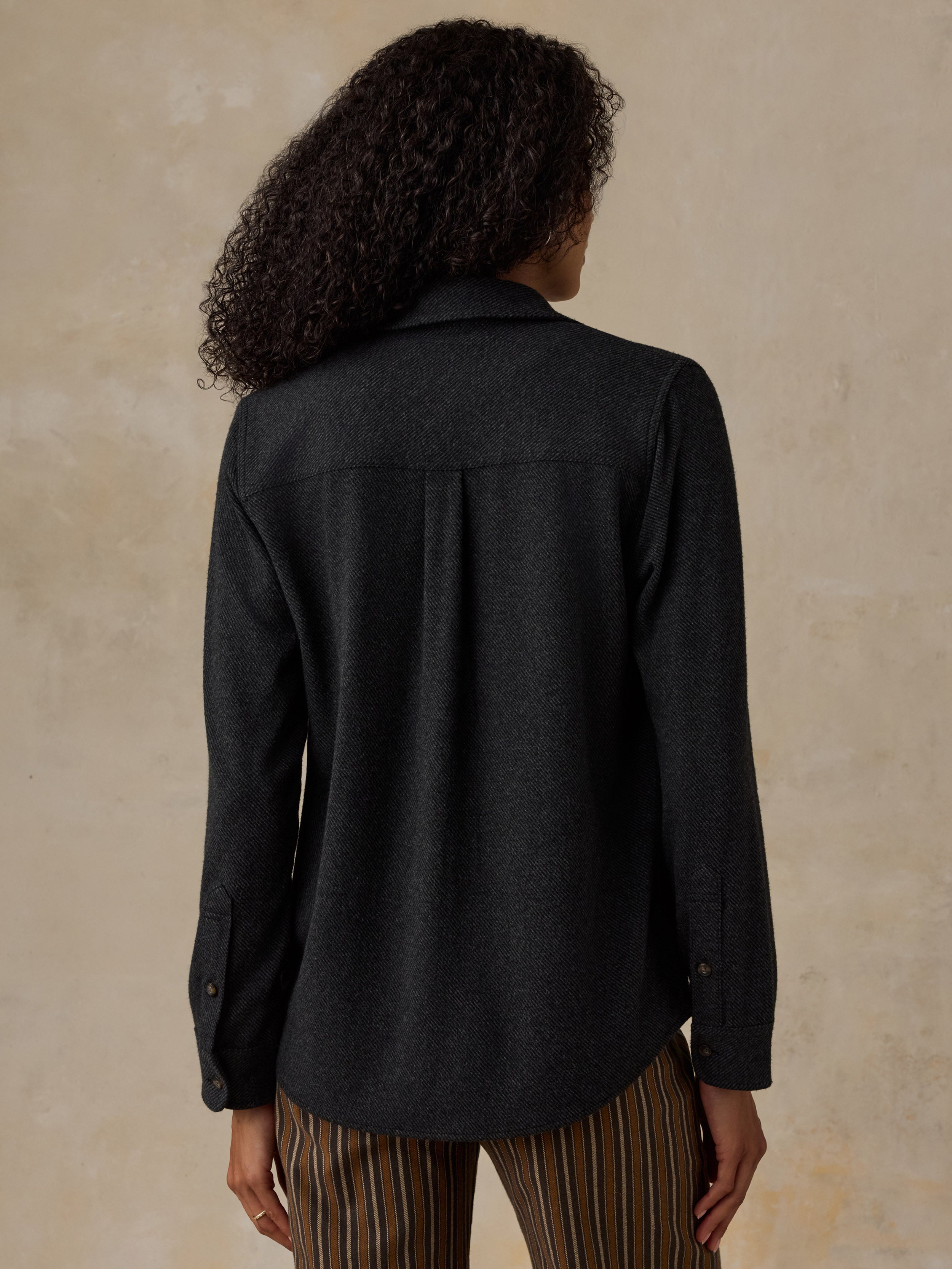 Woman wearing a black sweater shirt with brown striped pants against a beige background