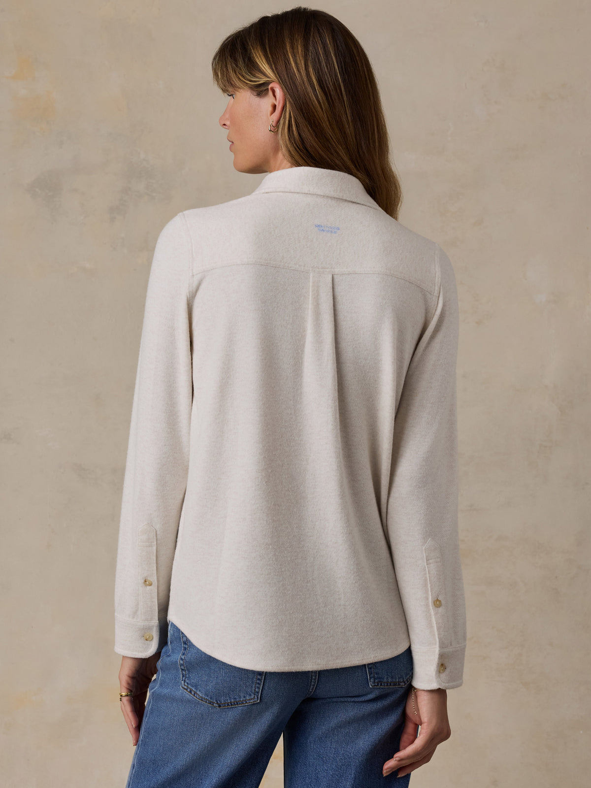 A woman viewed from behind wearing a white shirt and blue jeans, image 4 of 7