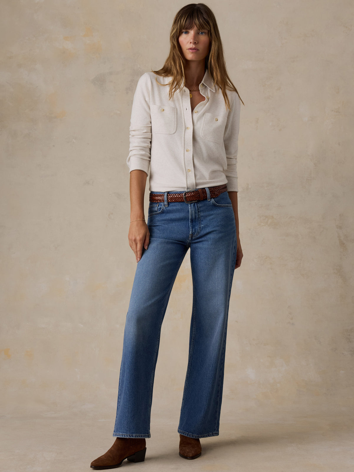 A woman wearing a white shirt, blue jeans, and brown boots, image 2 of 7