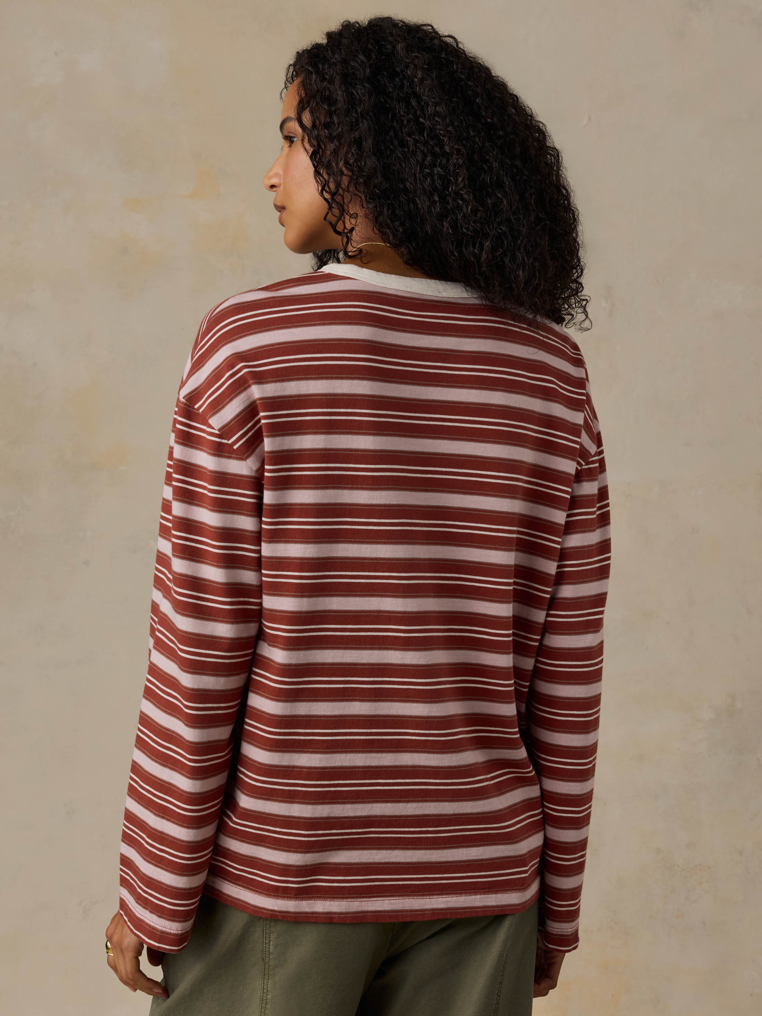 Woman wearing a red and pink striped long-sleeve shirt and green pants against a beige background