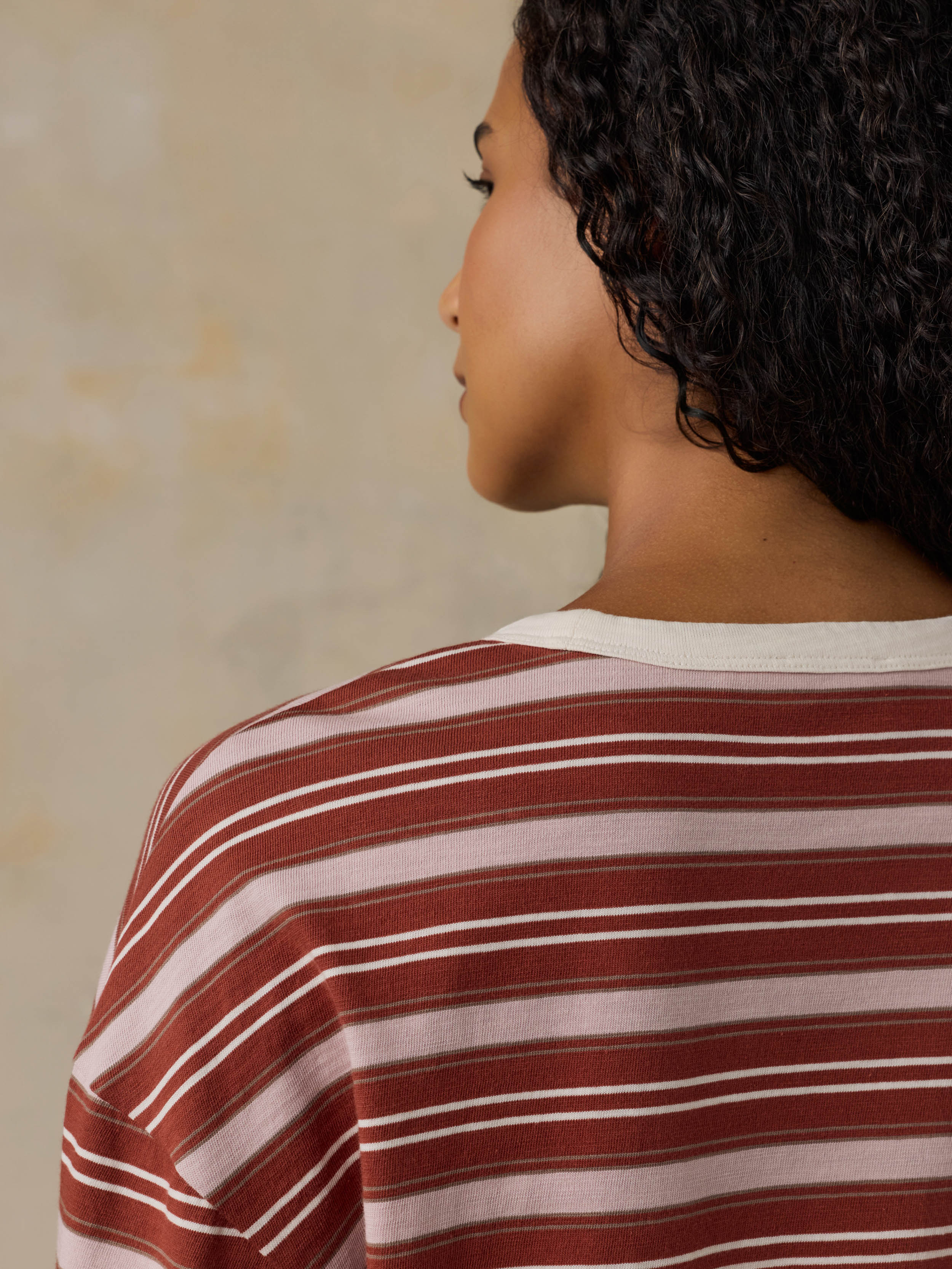 Woman wearing a red and pink striped long-sleeve shirt against a beige background
