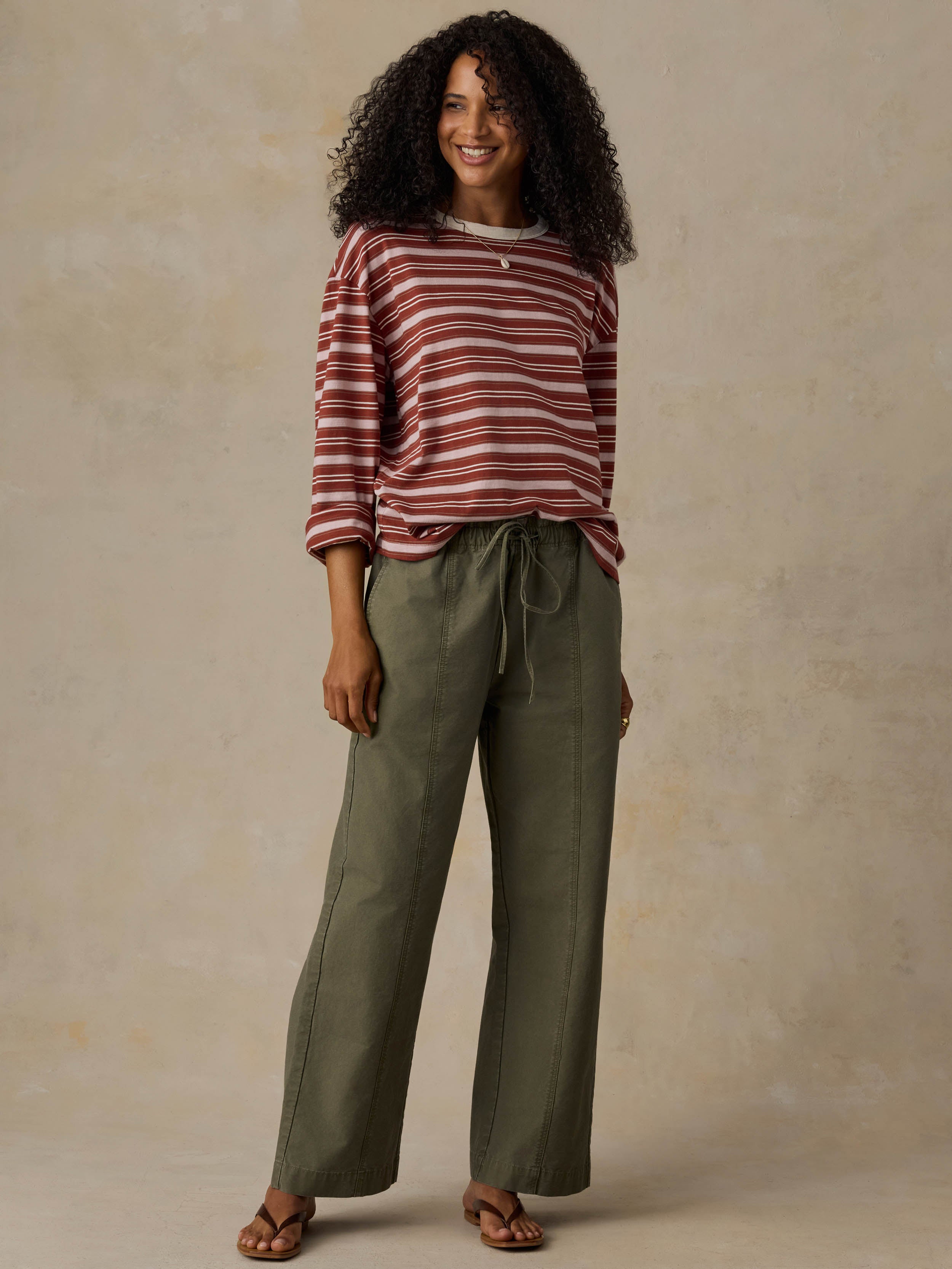 Woman wearing a red and pink striped long-sleeve shirt and green pants against a beige background