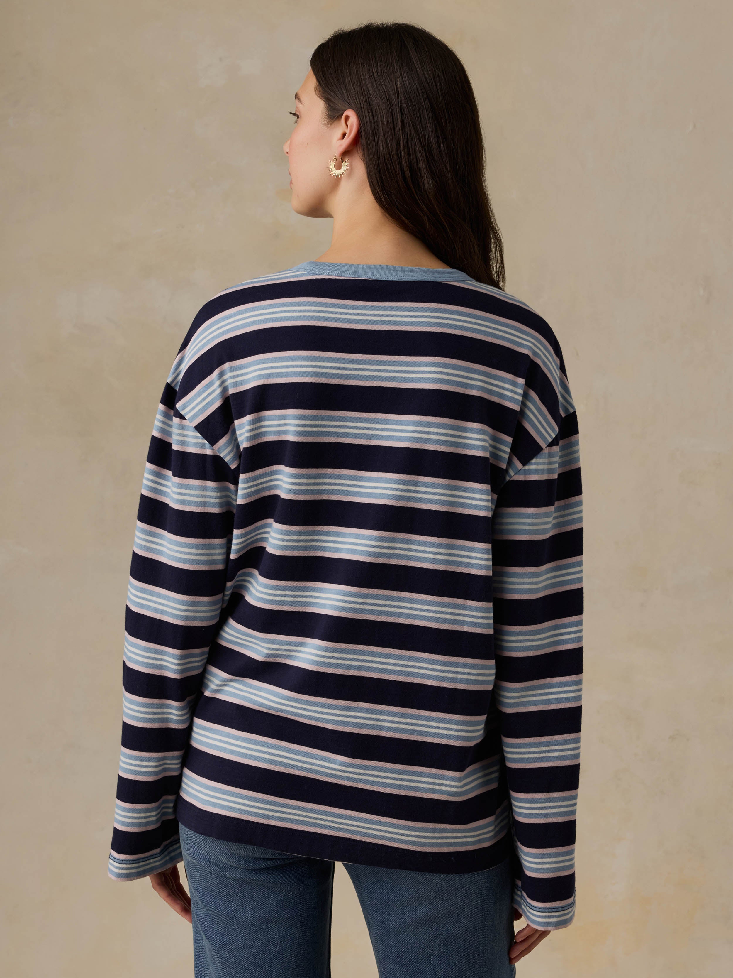 Woman wearing a blue striped shirt and jeans against a beige background