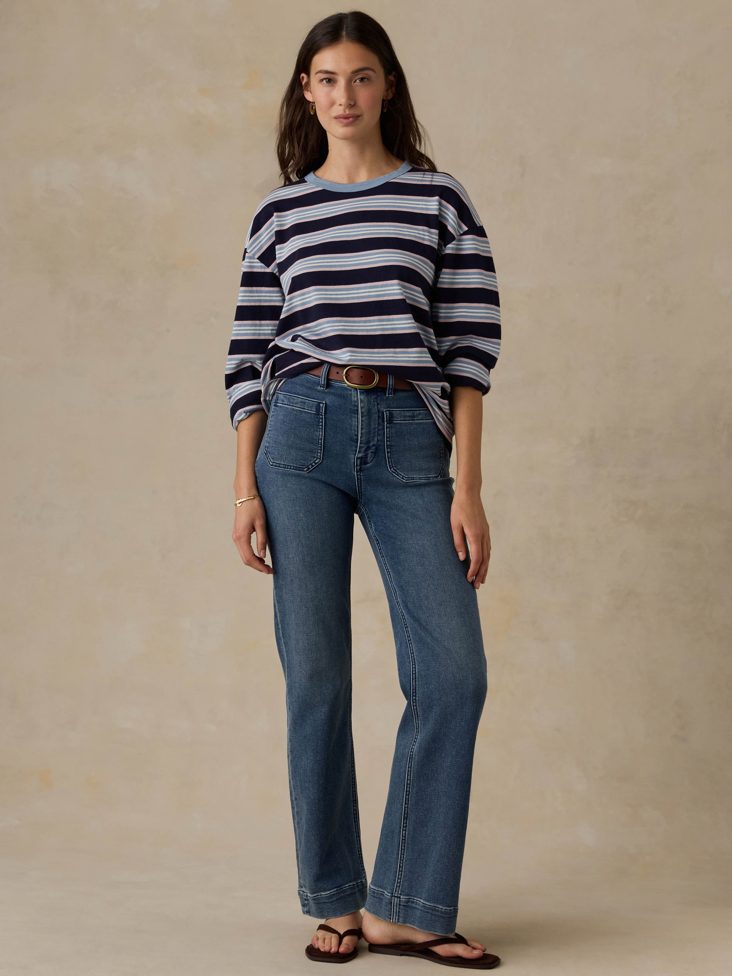 Woman wearing a blue striped shirt and jeans against a beige background