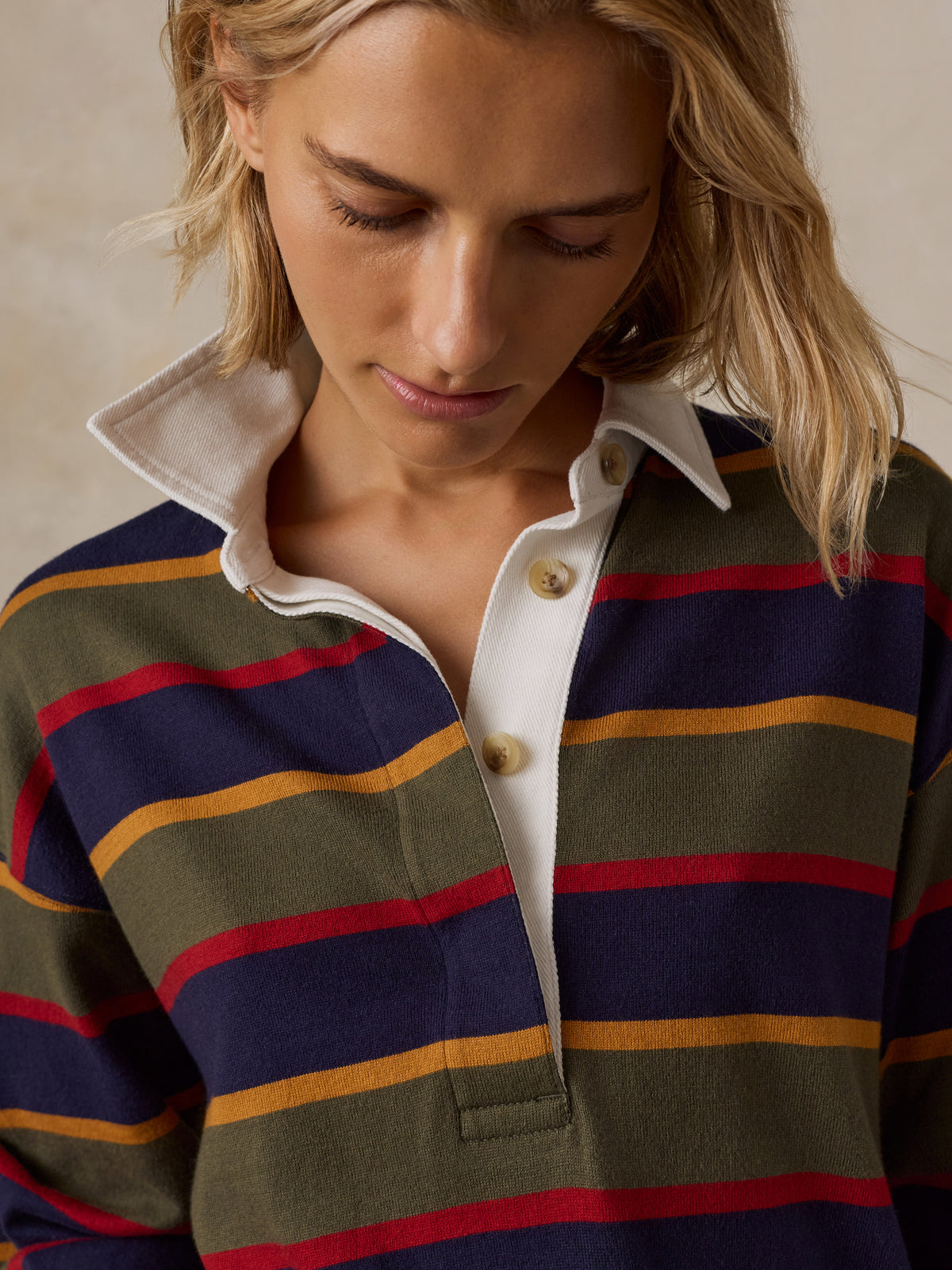 A woman wearing a long-sleeve rugby-style shirt with stripes in olive green, navy blue, red, and mustard yellow, image 2 of 7