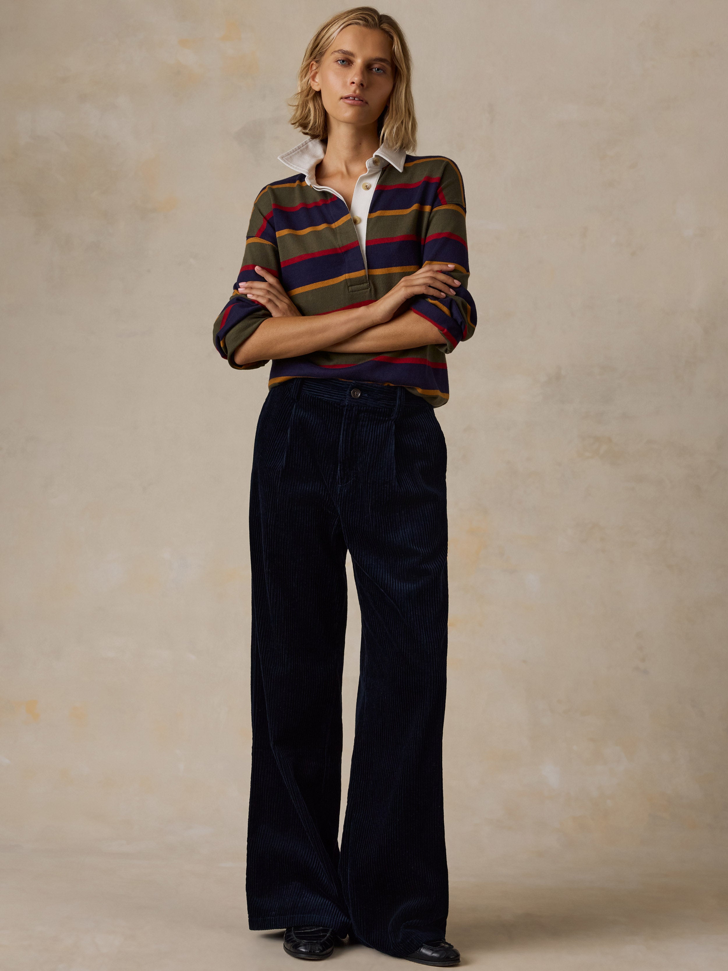 A woman wearing a long-sleeve rugby-style shirt with stripes in olive green, navy blue, red, and mustard yellow