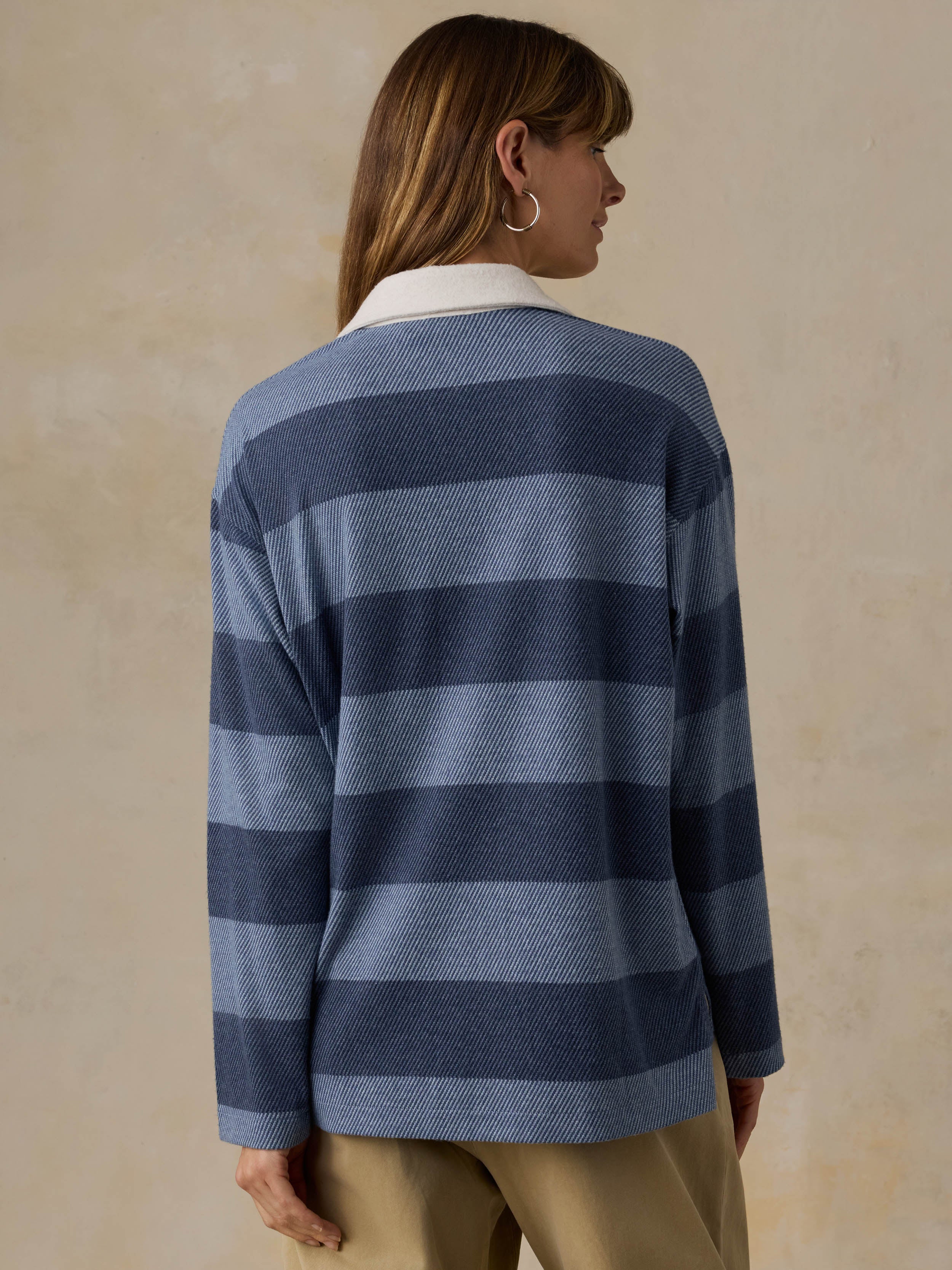 Woman wearing a blue striped rugby shirt with beige pants against a beige background
