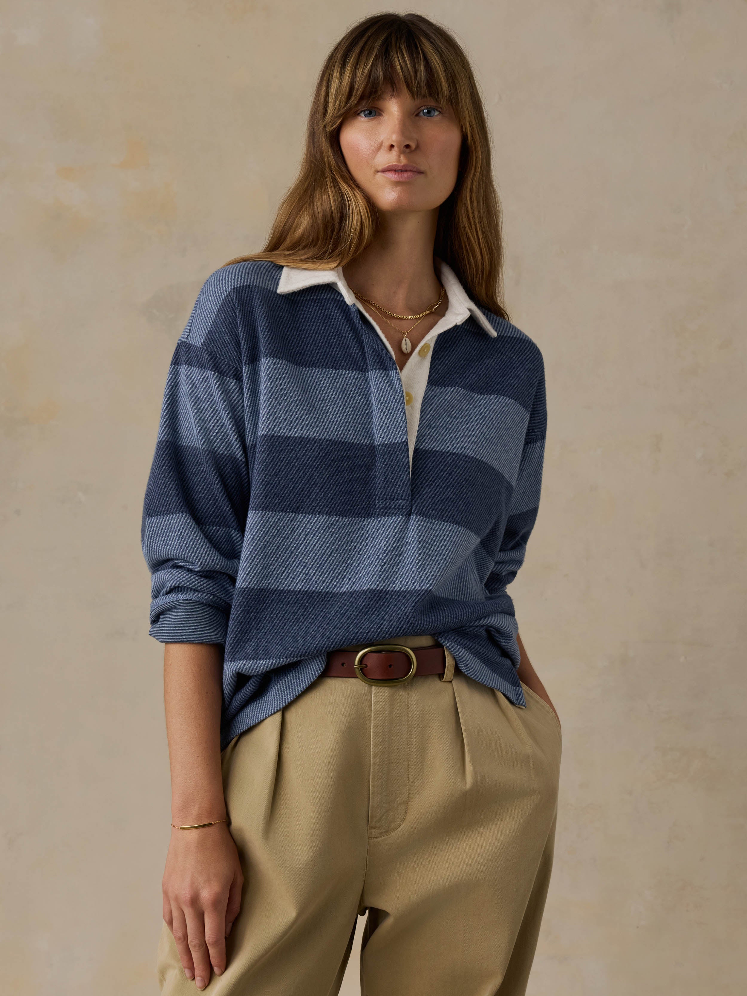 Woman wearing a blue striped rugby shirt with beige pants against a beige background
