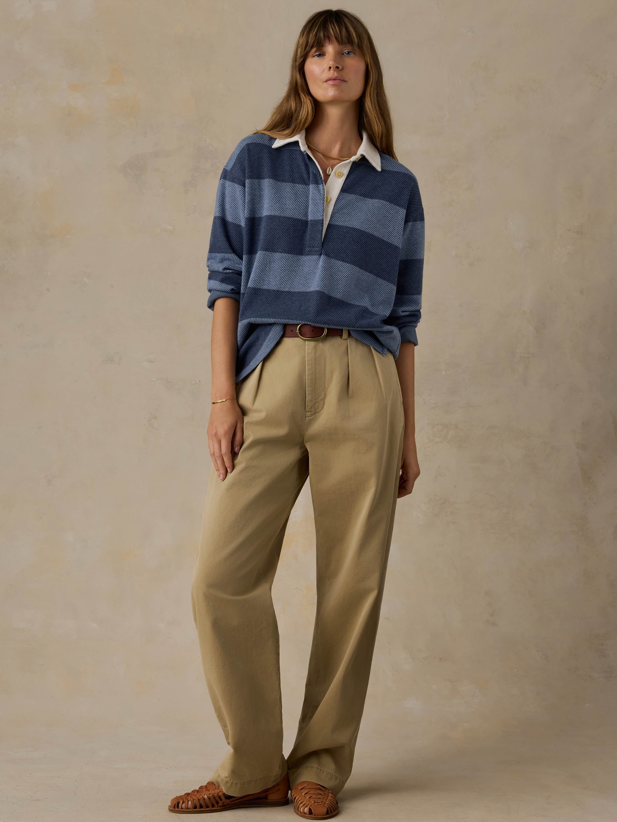 Woman wearing a blue striped rugby shirt with beige pants against a beige background