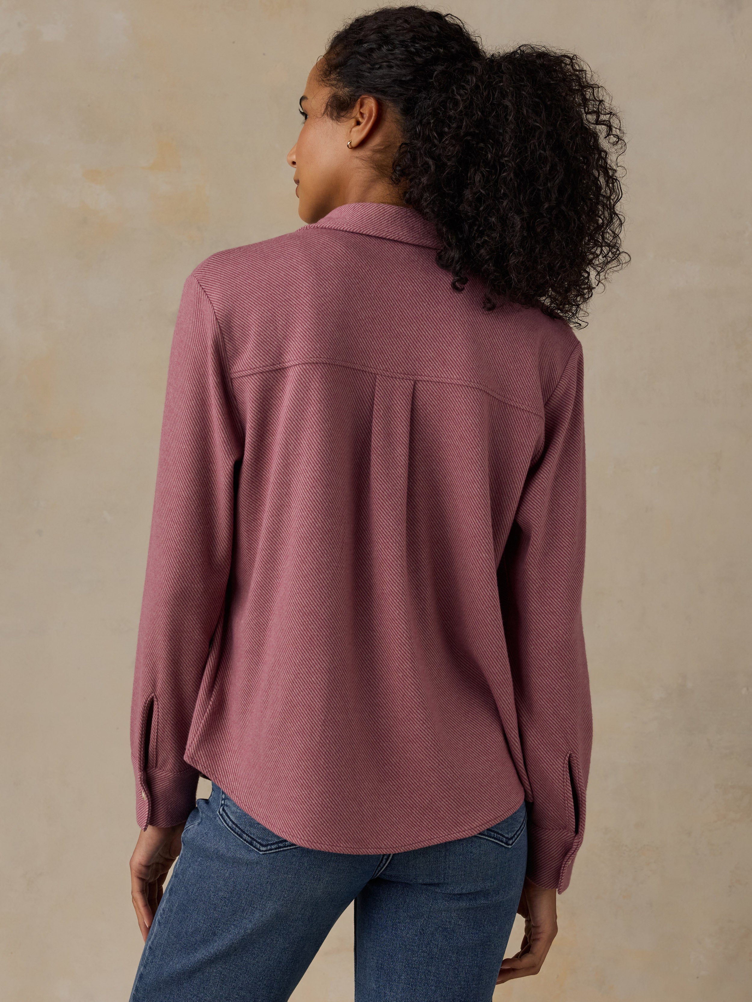Woman wearing a pink button down shirt and blue jeans against a beige background
