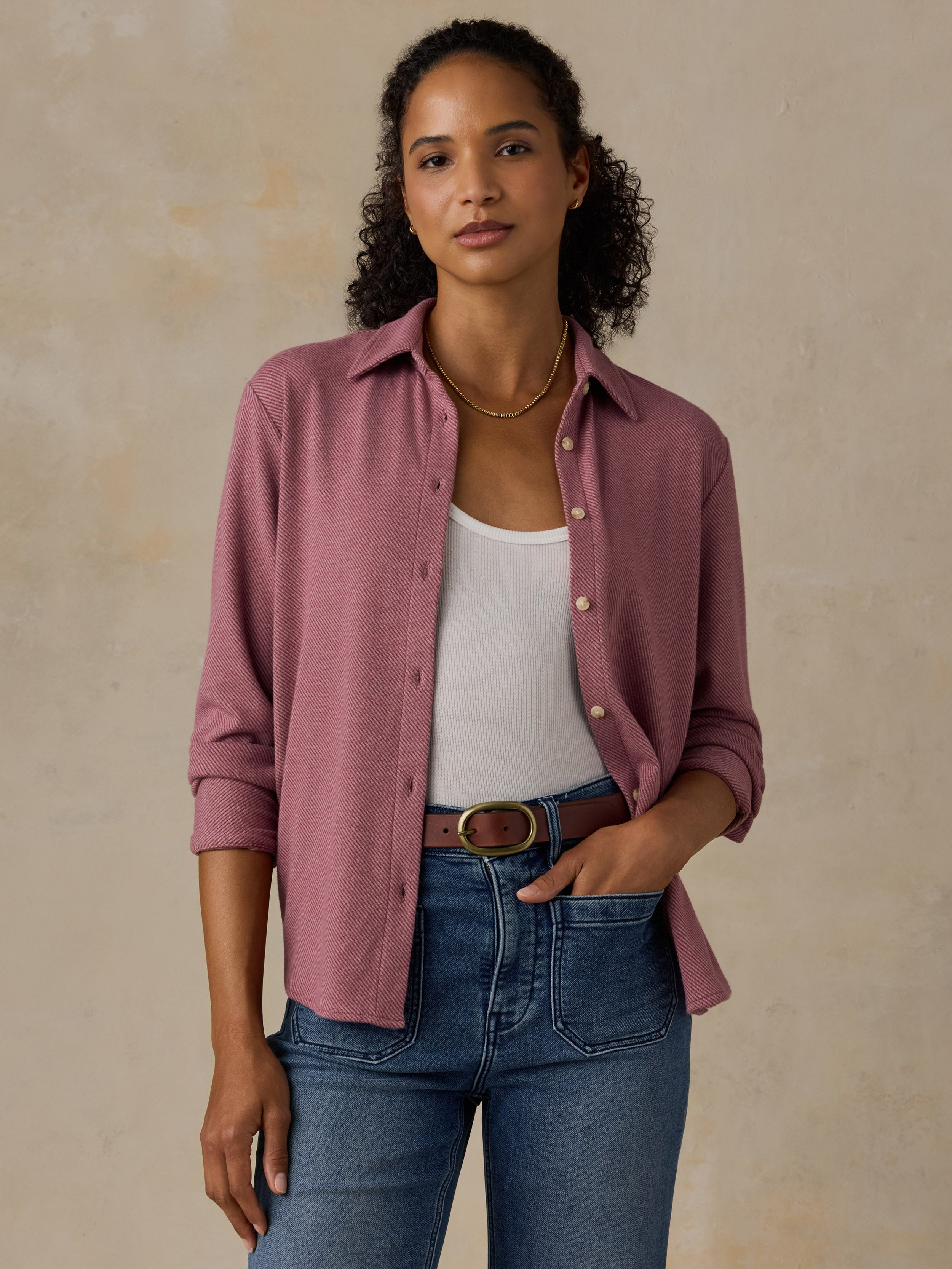 Woman wearing a pink button down shirt and blue jeans against a beige background