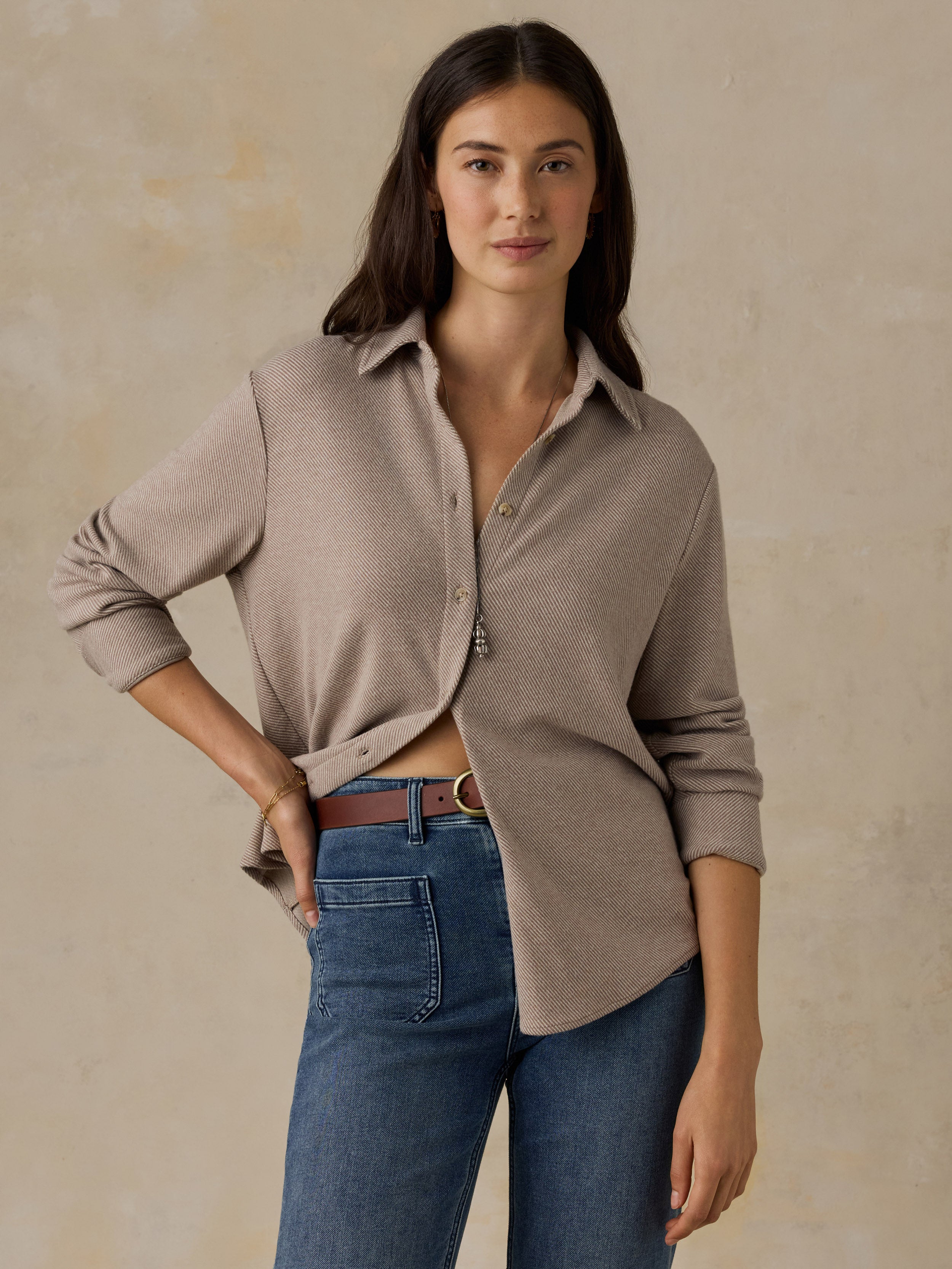 Woman wearing a beige button down shirt and blue jeans against a beige background