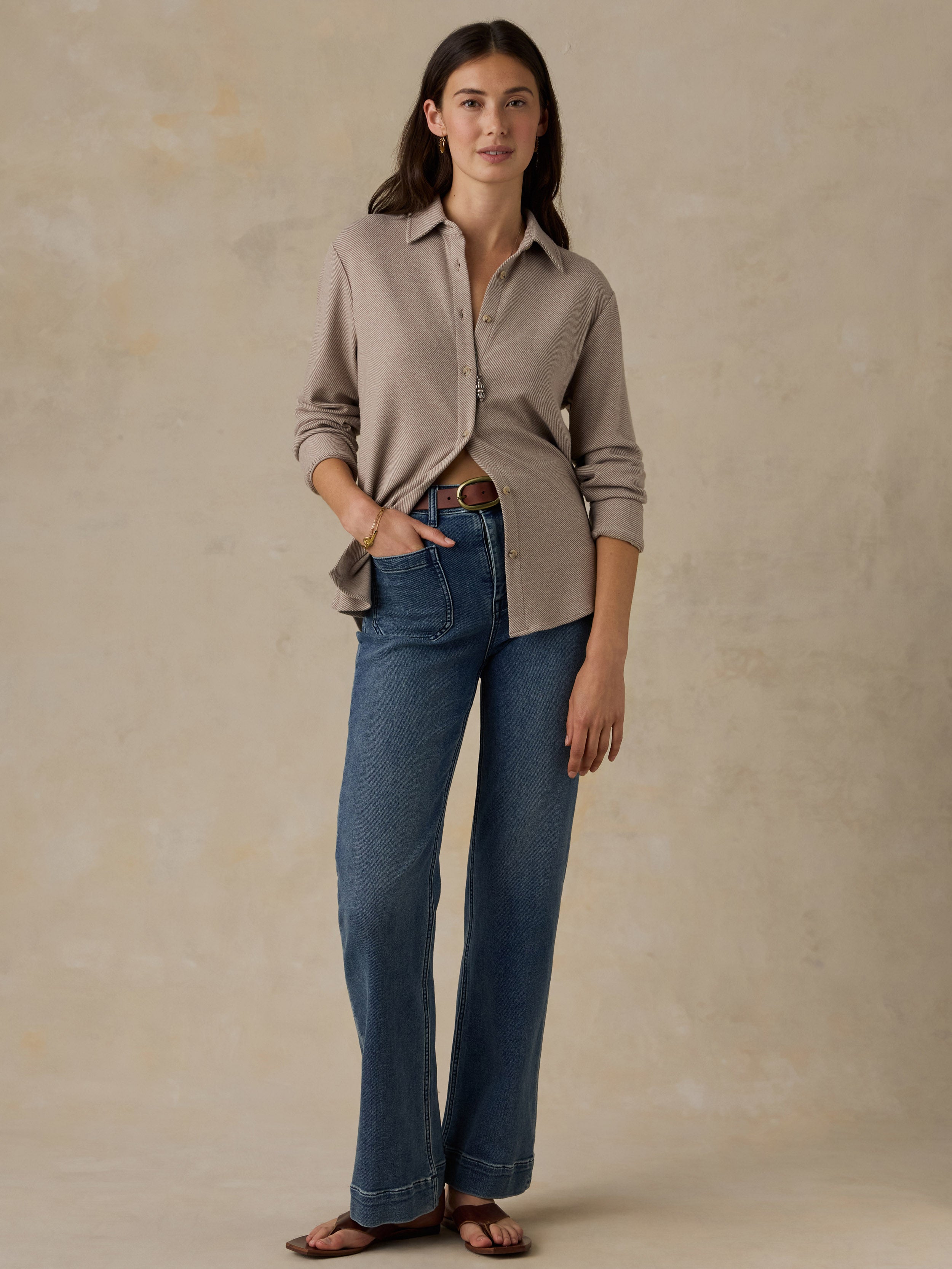 Woman wearing a beige button down shirt and blue jeans against a beige background
