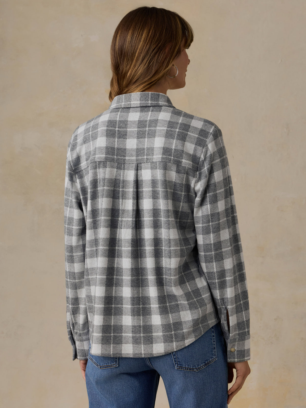 Woman wearing a grey plaid button down shirt and blue jeans against a beige background, image 3 of 6