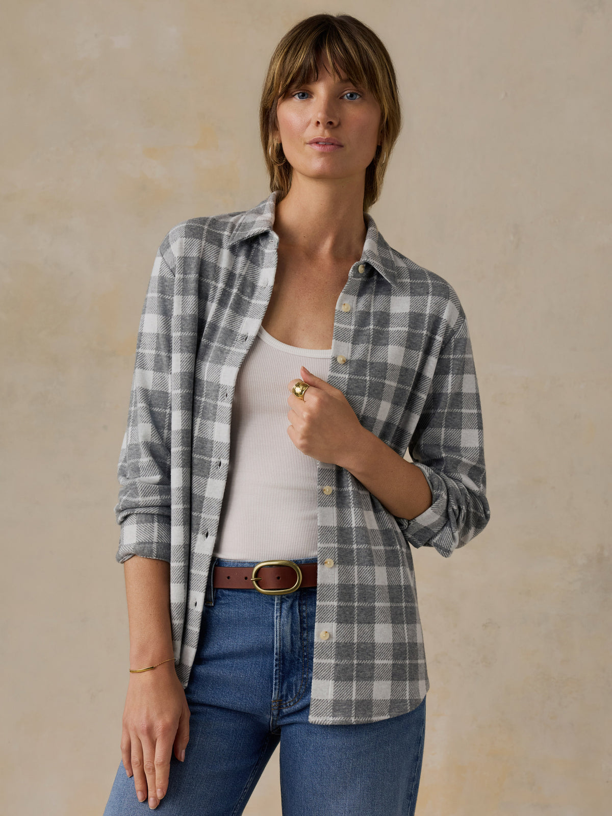 Woman wearing a grey plaid button down shirt and blue jeans against a beige background, image 1 of 6