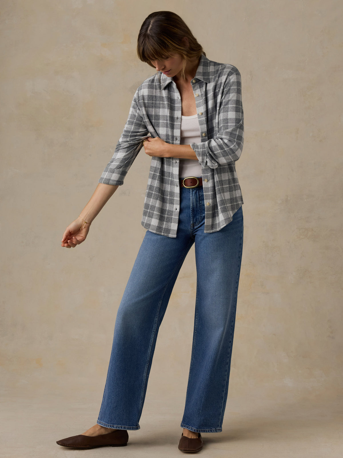 Woman wearing a grey plaid button down shirt and blue jeans against a beige background, image 4 of 6
