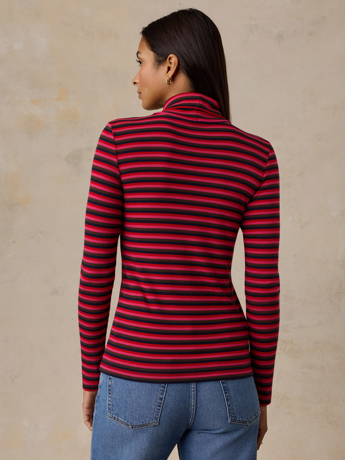 A woman viewed from behind wearing a red striped turtleneck and jeans, image 4 of 6