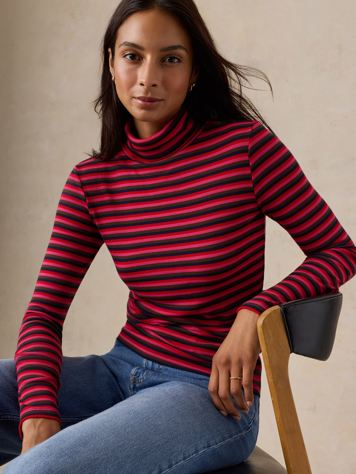 A woman wearing a red striped turtleneck and jeans, image 5 of 6