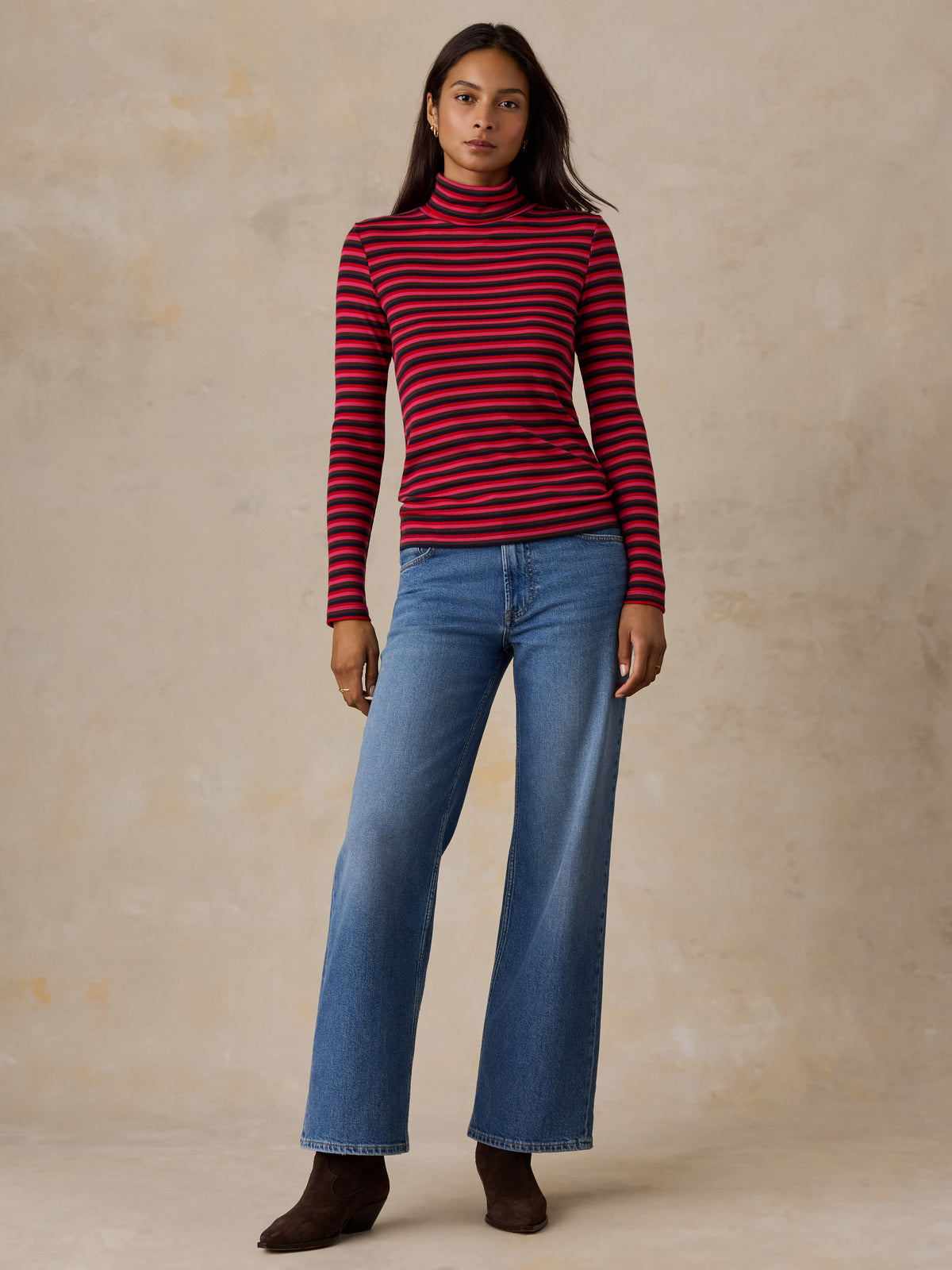 A woman wearing a red striped turtleneck and jeans, image 3 of 6