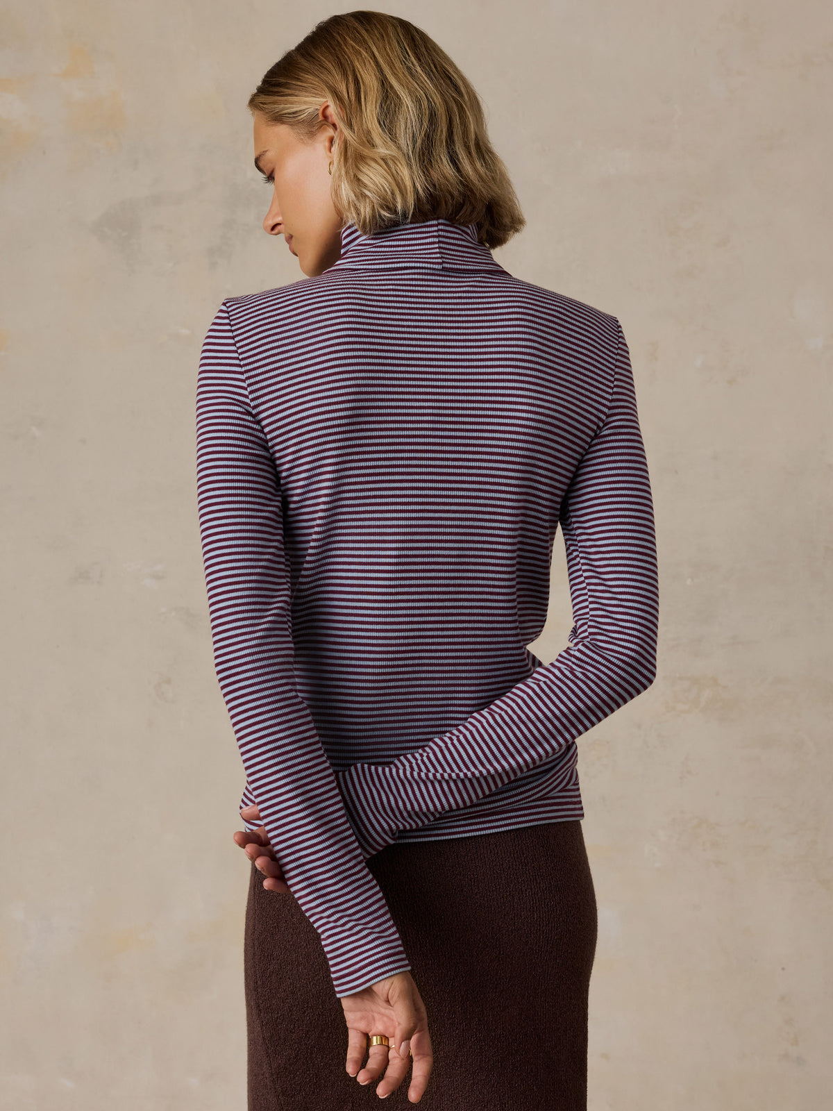 A woman viewed from behind wearing a blue striped turtleneck and brown skirt, image 4 of 6