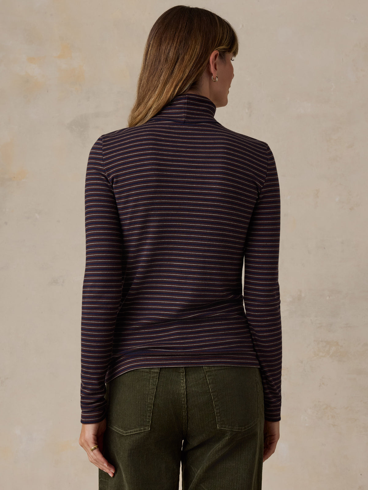 A woman wearing a brown striped turtleneck and green corduroy pants, image 5 of 6