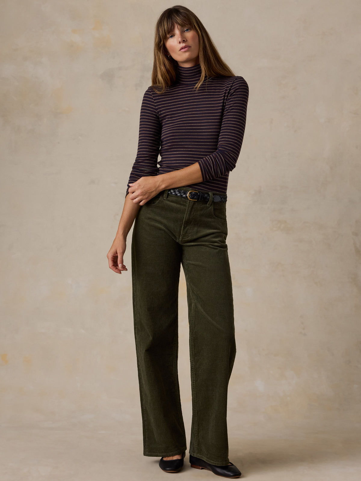 A woman wearing a brown striped turtleneck and green corduroy pants, image 3 of 6