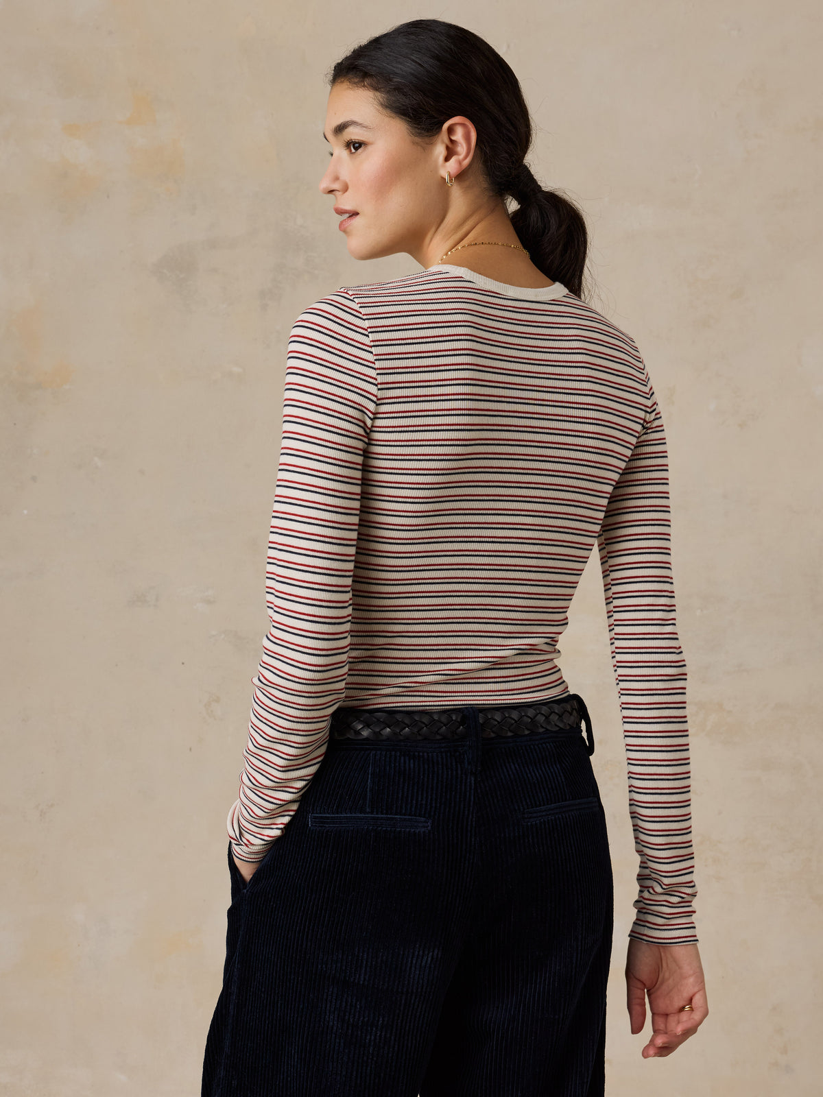 A woman viewed from behind wearing a striped shirt and dark pants, image 5 of 6