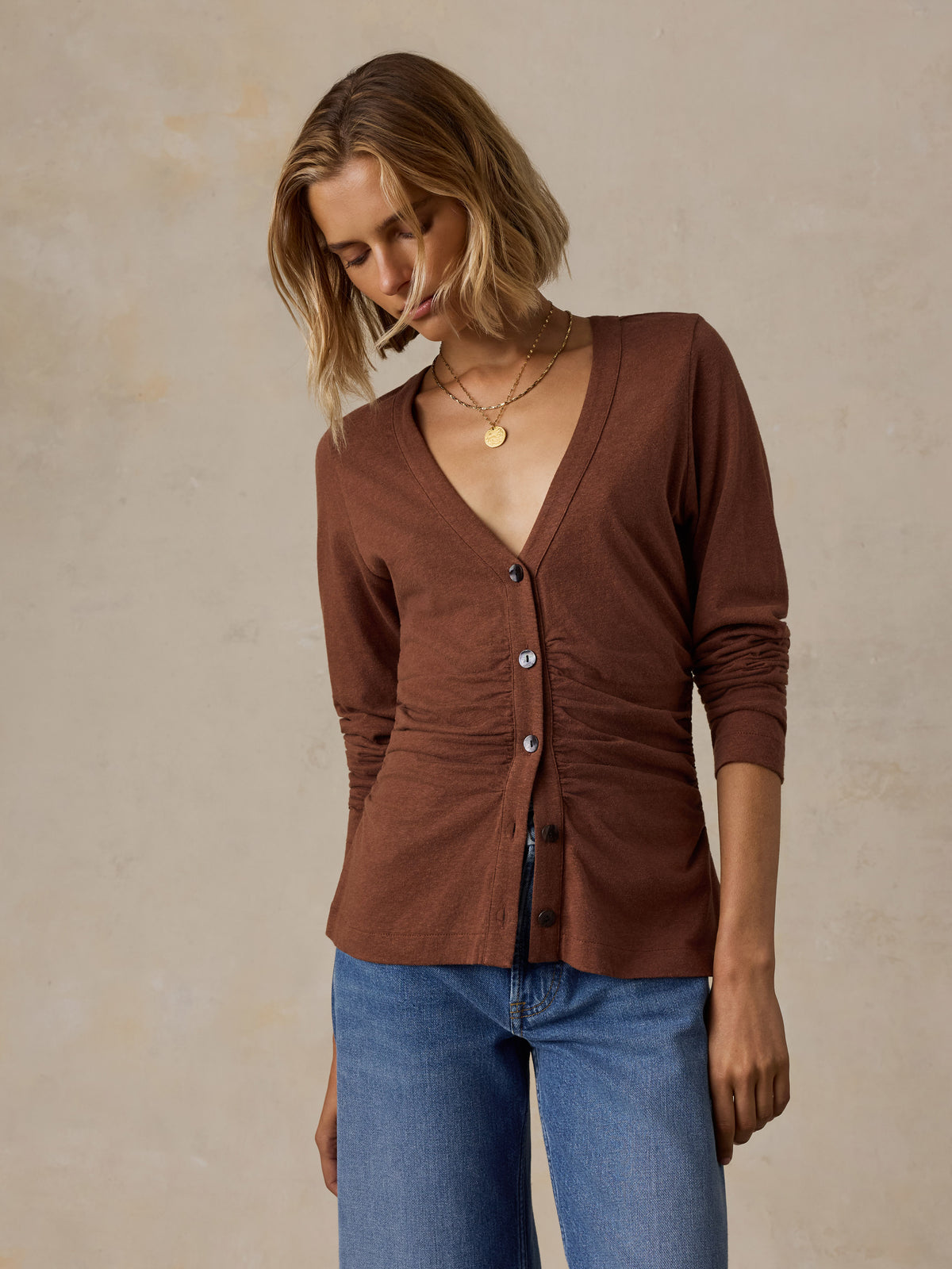 A woman wearing a brown long sleeve top and blue jeans, image 6 of 6