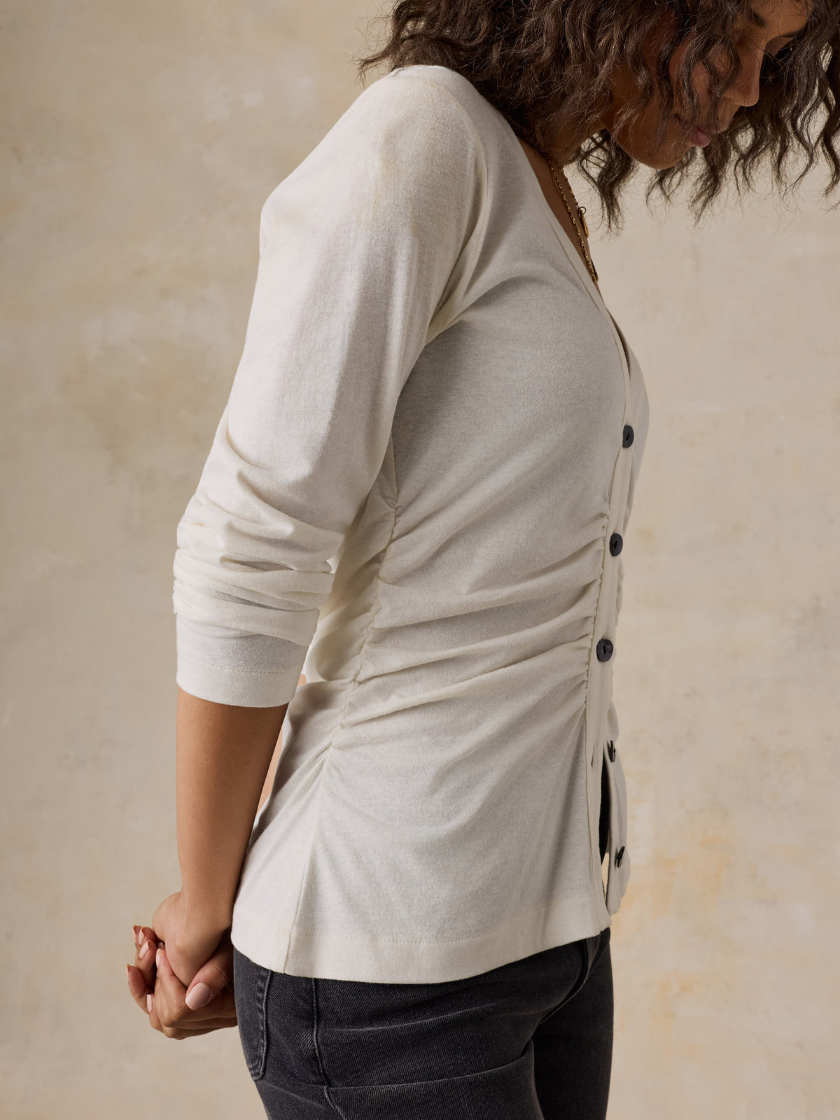 A woman wearing a white cardigan and black jeans, image 6 of 6