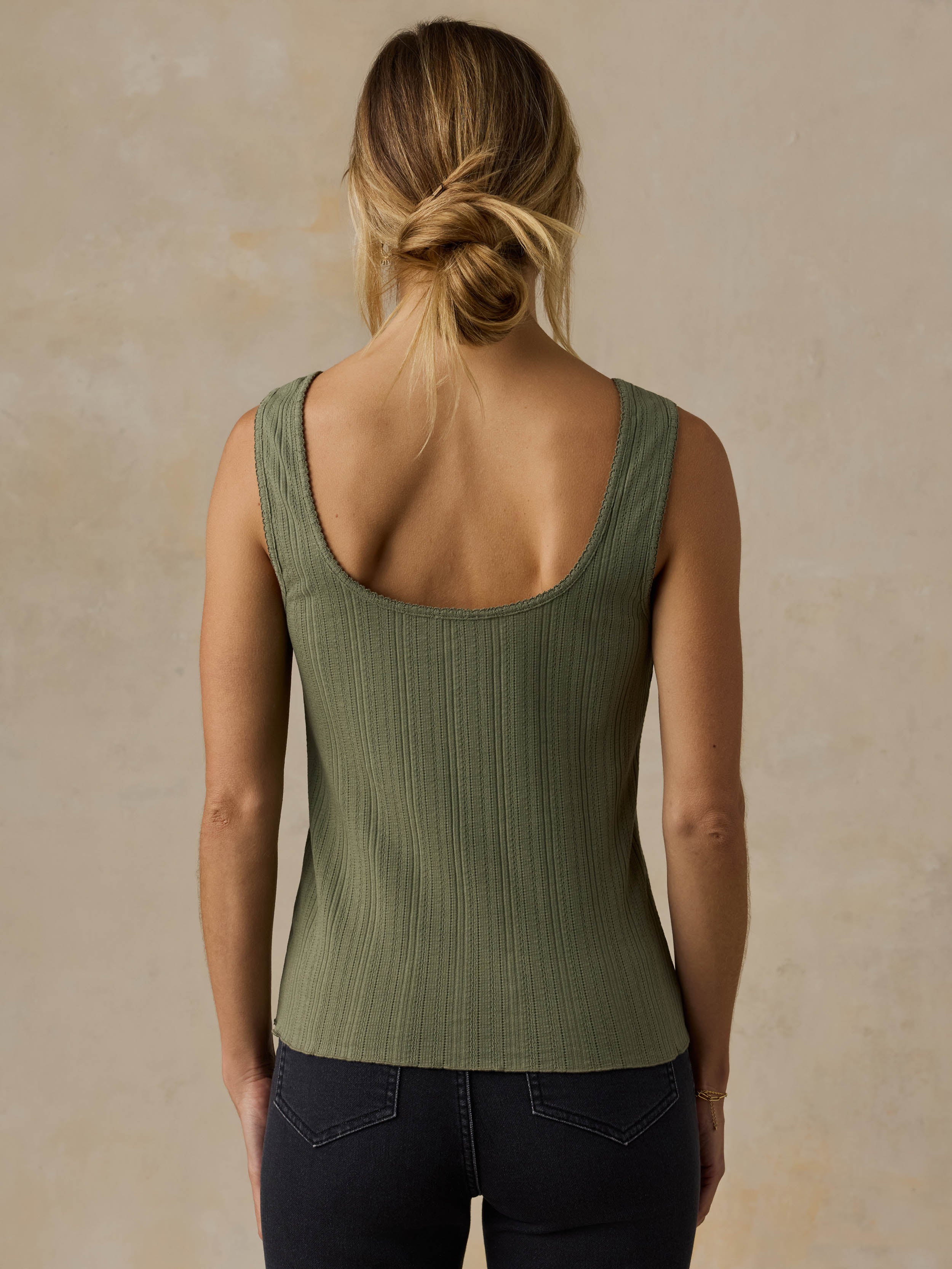Woman wearing a green tank top and black jeans against a beige background