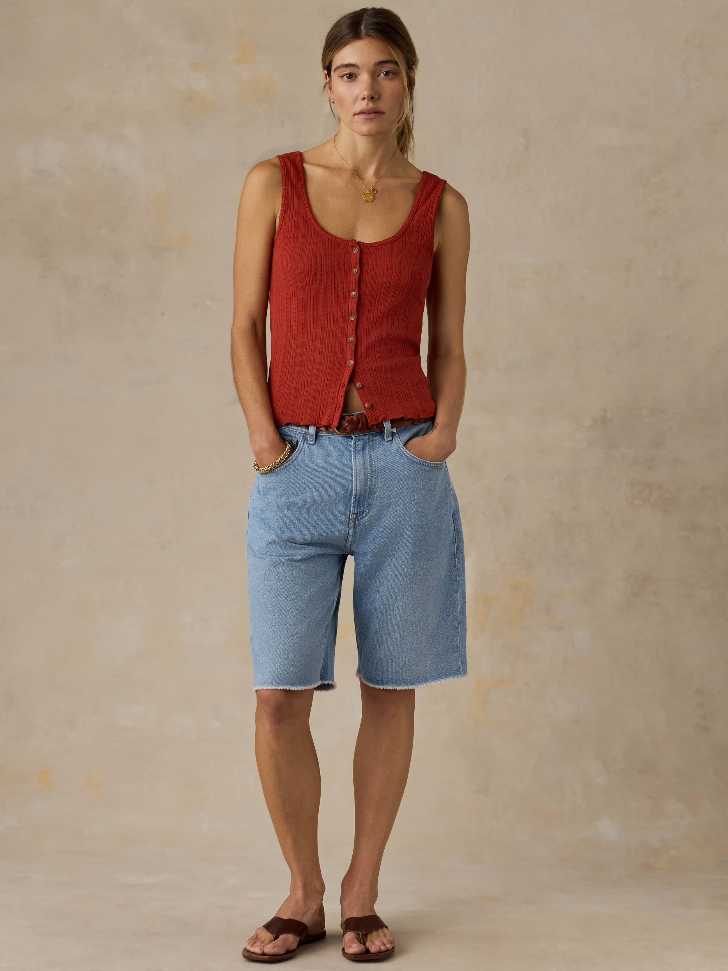 Woman wearing a red tank top and blue jeans against a beige background